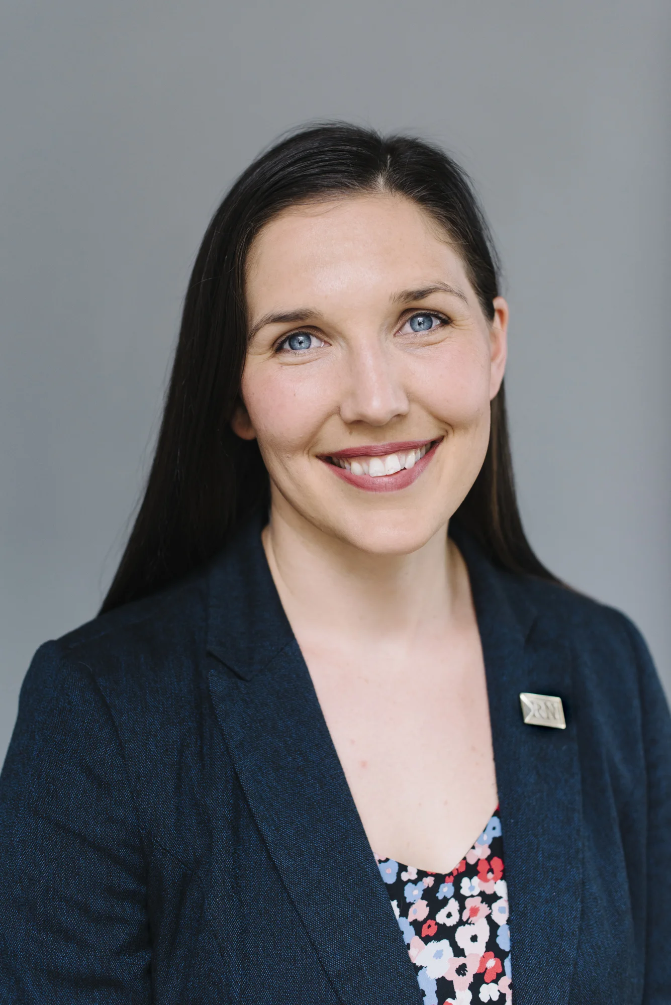 Studio headshot of a woman in a blazer and colourful floral shirt against a clean grey backdrop in Toronto