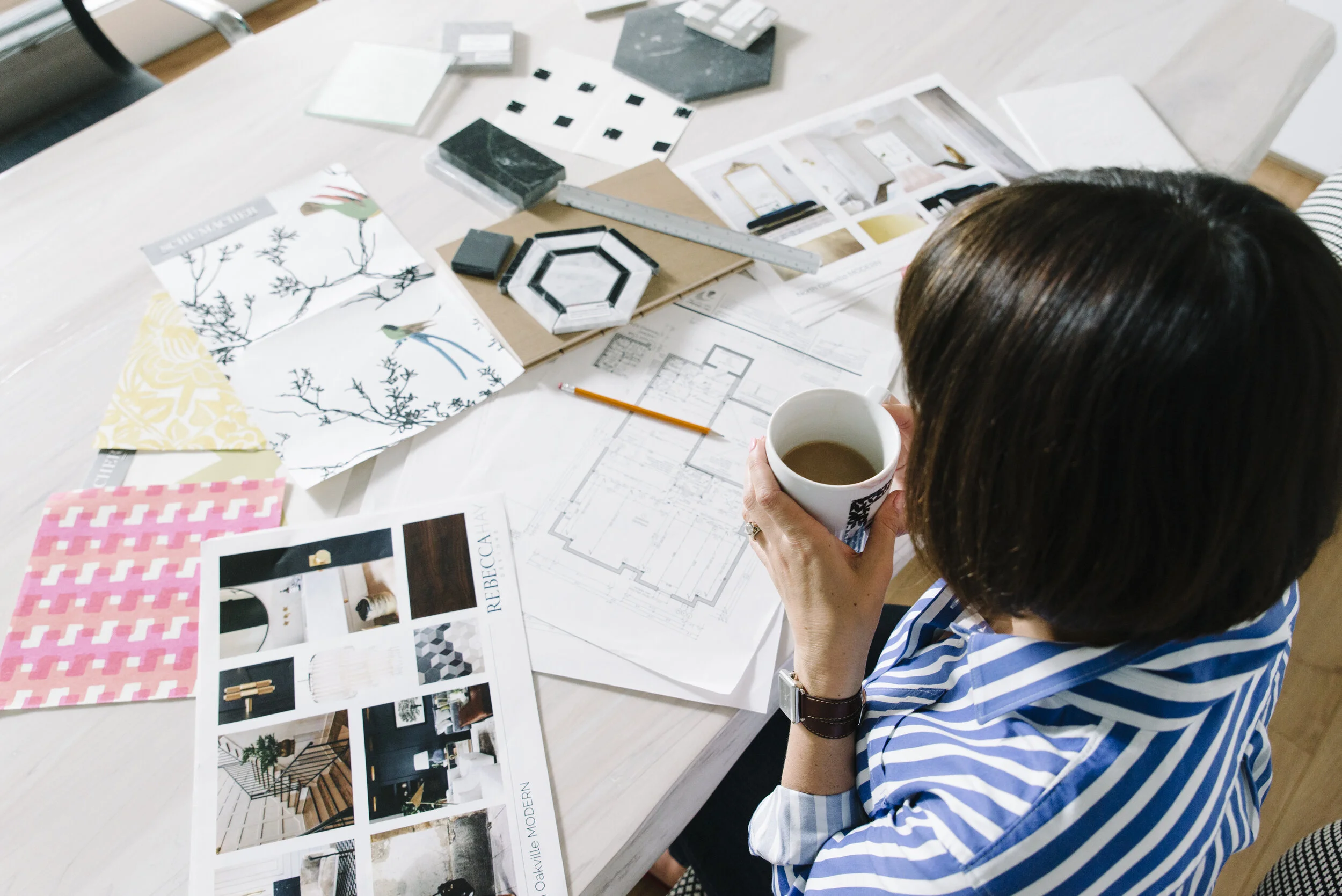 Over the shoulder lifestyle photo of Rebecca Hay holding a coffee with a design board and fabric textiles spread out in front of her