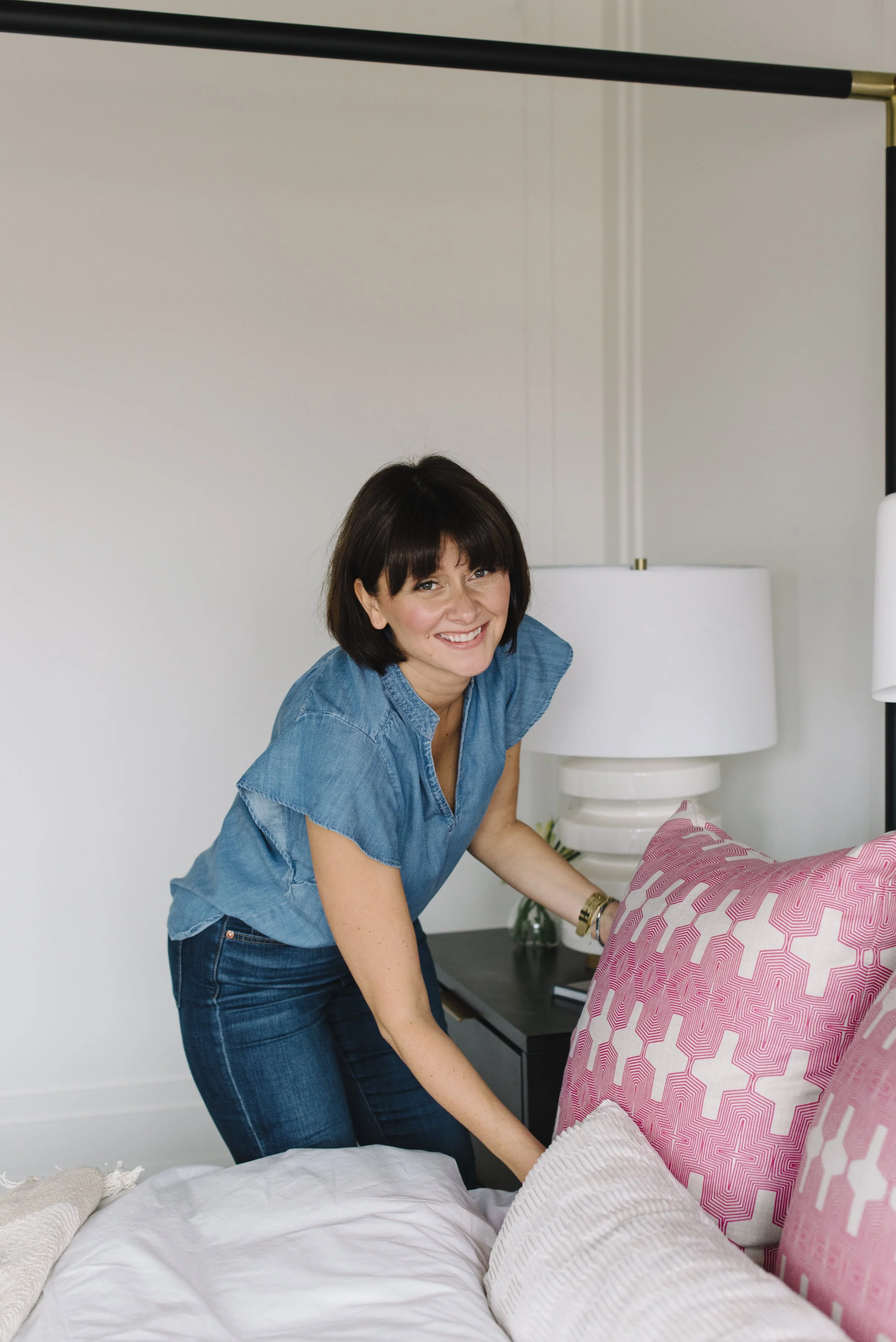Candid lifestyle branding photo of Rebecca Hay making a bed and smiling at the camera in a designed interior space