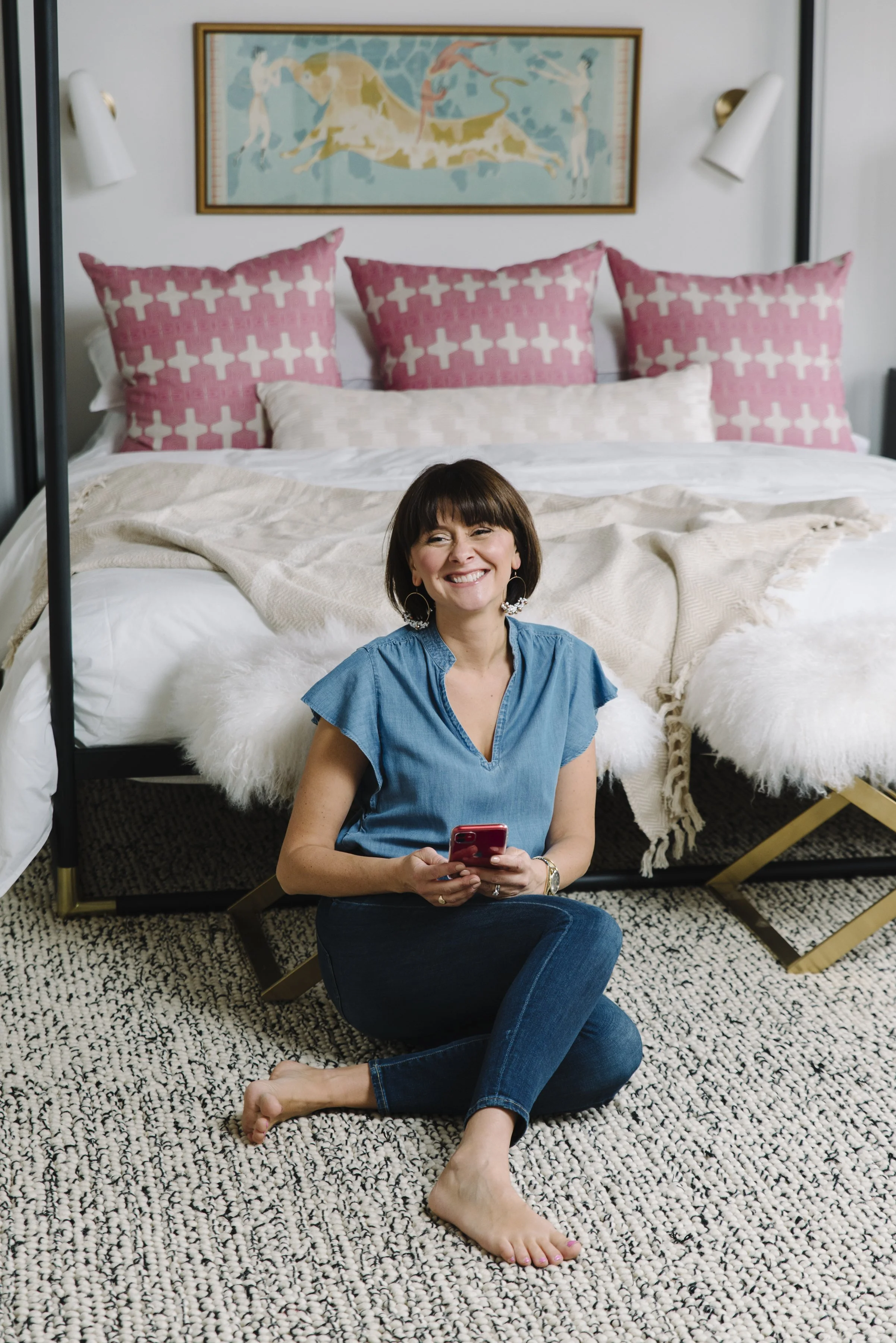 Lifestyle branding photo of Rebecca Hay sitting at the foot of a bed working on her phone in a styled interior space