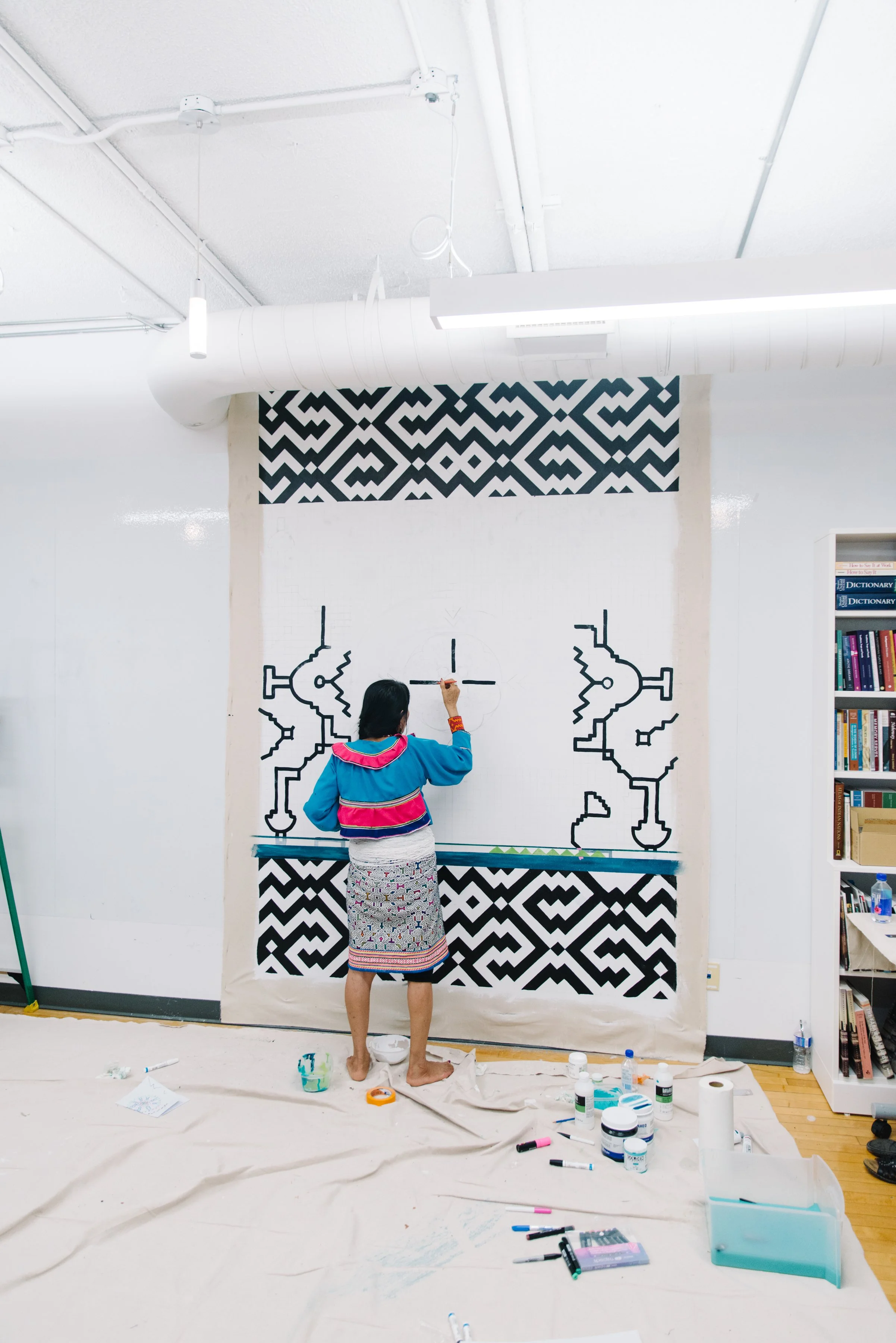 Wide portrait of Indigenous Amazon artist Olinda Reshinjabe Silvano painting the Paisajes de Nosotros mural at Toronto Metropolitan University