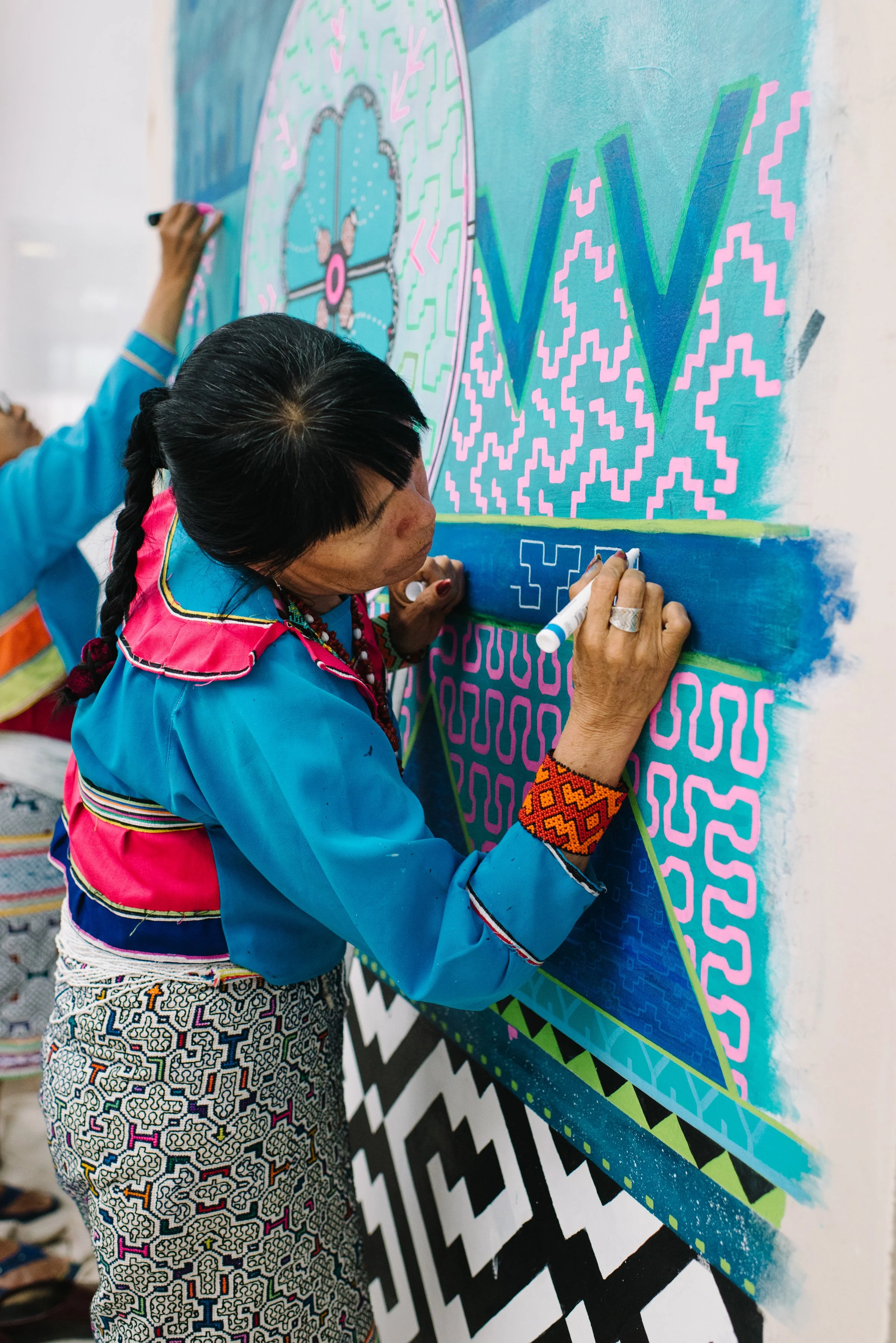 Close portrait of Olinda Reshinjabe Silvano working in front of the nearly completed Paisajes de Nosotros mural at TMU in Toronto