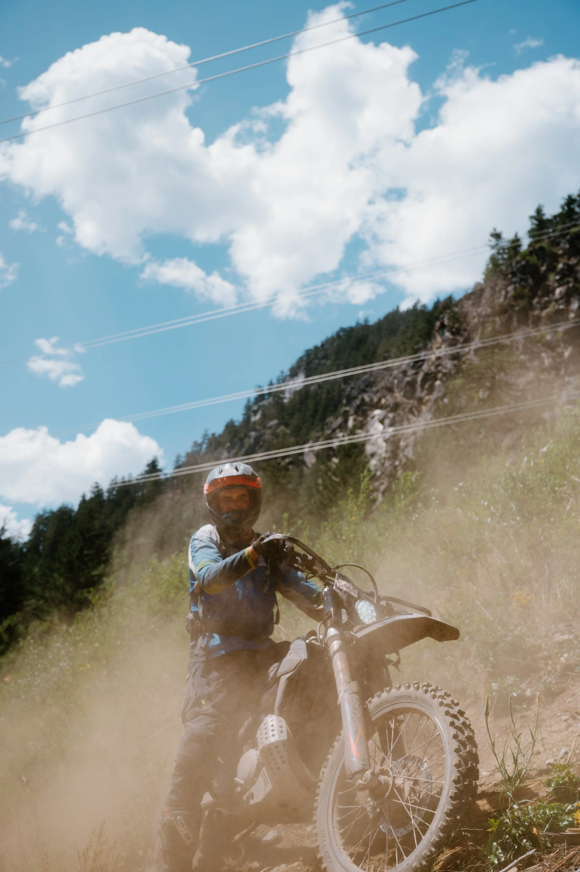 Portrait of a dirt bike rider climbing a trail in Pemberton BC with dust rising around him