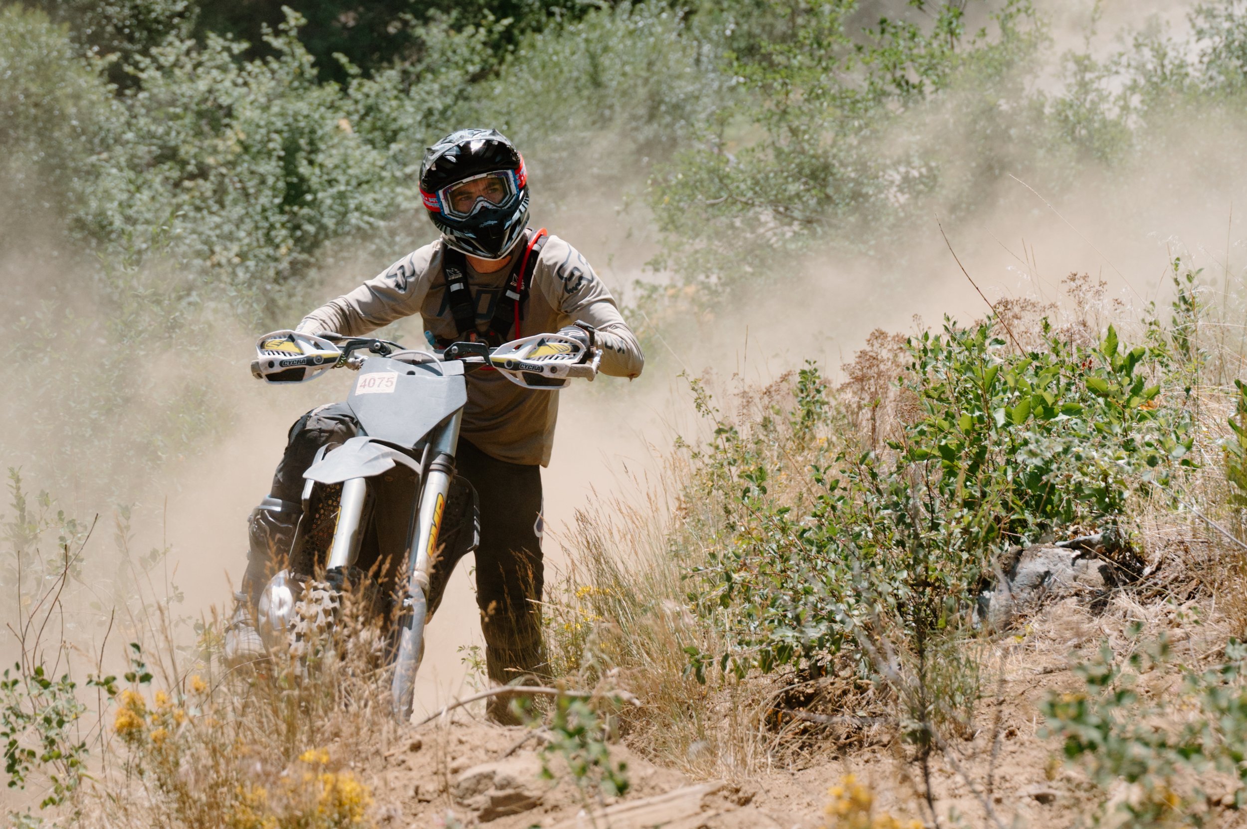 Atmospheric portrait of a dirt bike rider on a BC trail surrounded by heavy dust, editorial campaign style