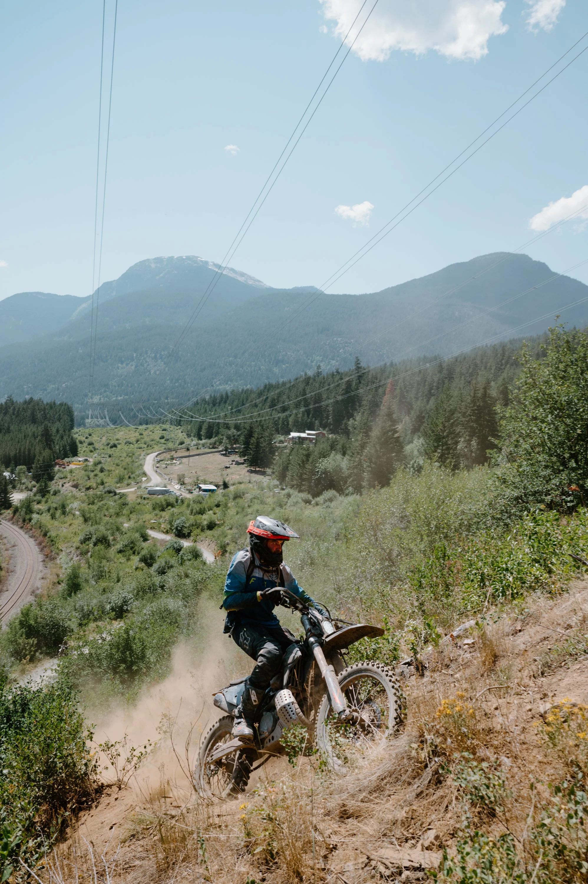 Dirt bike rider climbing a steep mountain trail in Pemberton BC with the expansive BC landscape behind him