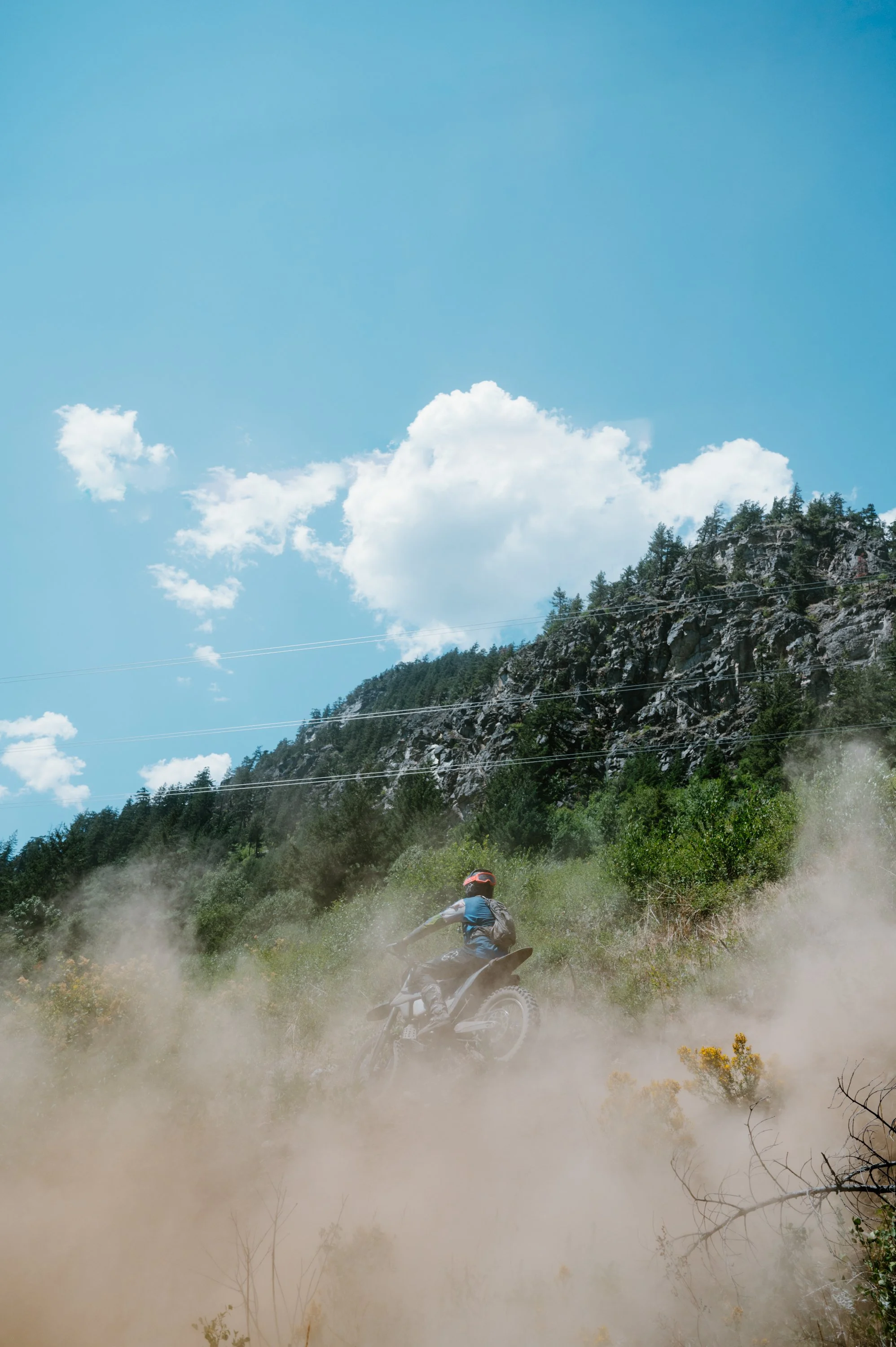Wide action photo of a dirt bike rider taking off on a dusty trail in Pemberton BC, suited for an alpine motocross or athletic apparel campaign