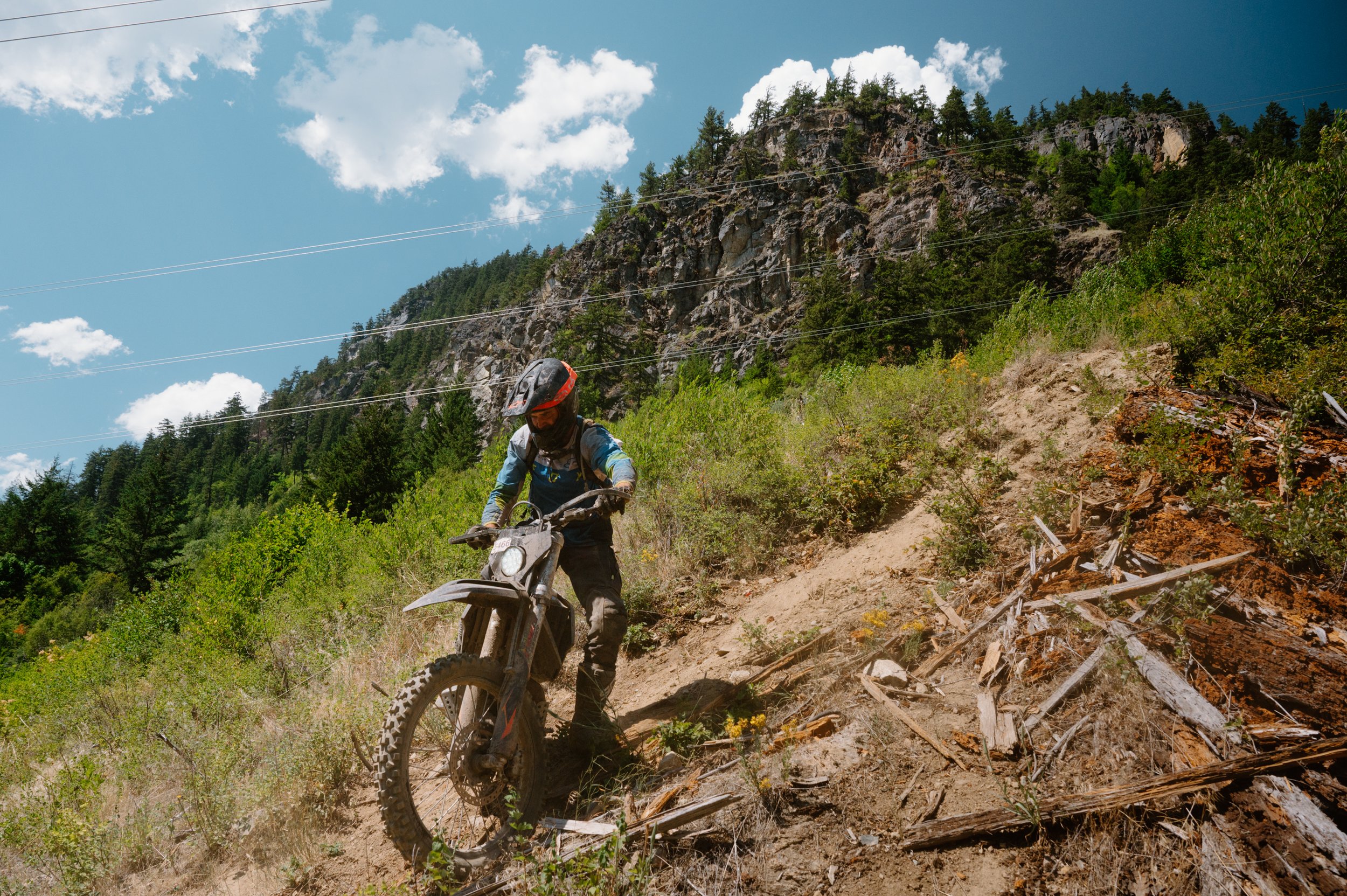 Dirt bike rider on a dusty trail in Pemberton BC with a dramatic mountain landscape in the background, suited for an athletic apparel campaign