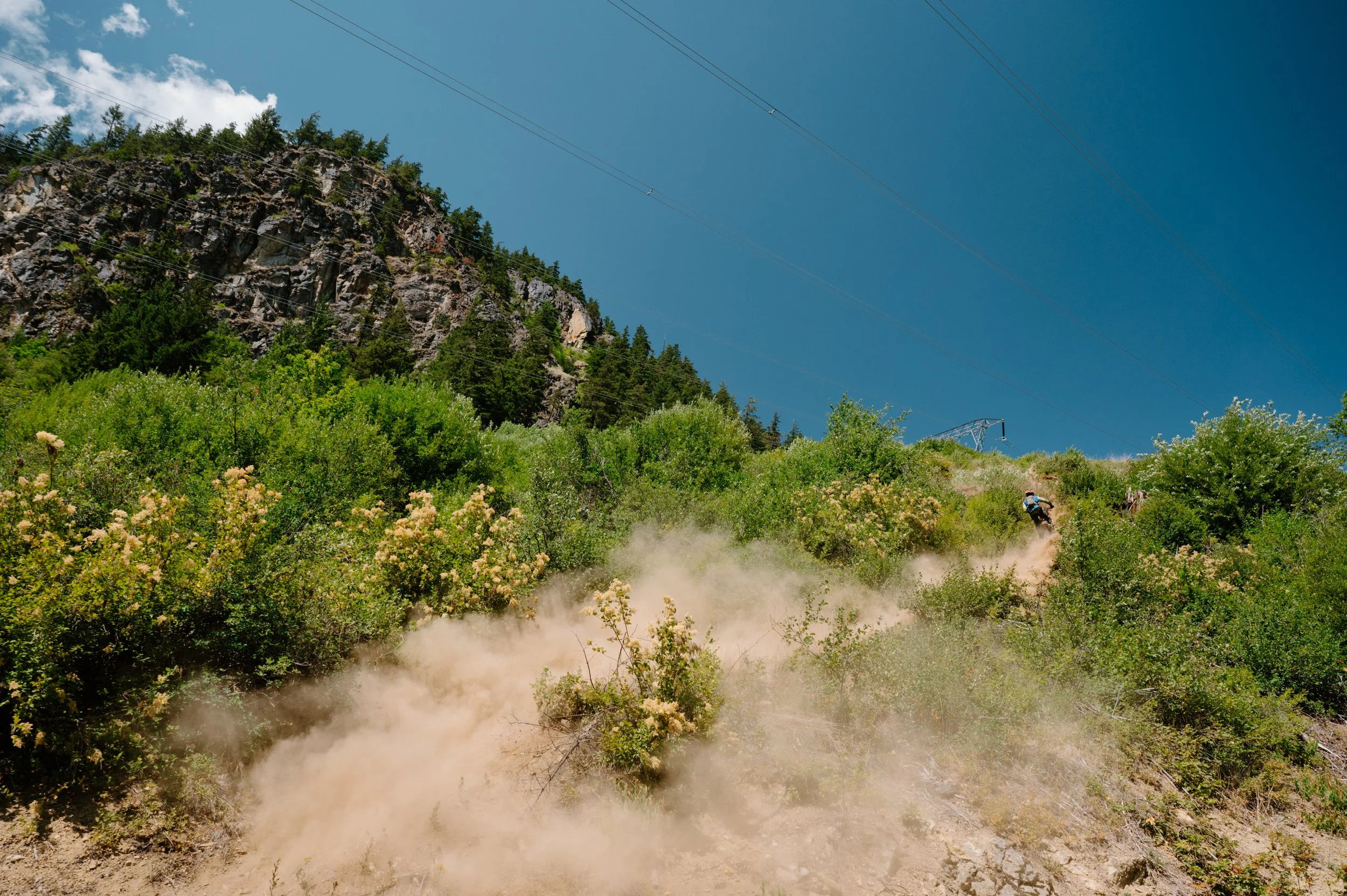 Very wide landscape photo of a dirt bike rider ascending a trail in Pemberton BC, emphasizing the dramatic scale of the BC terrain
