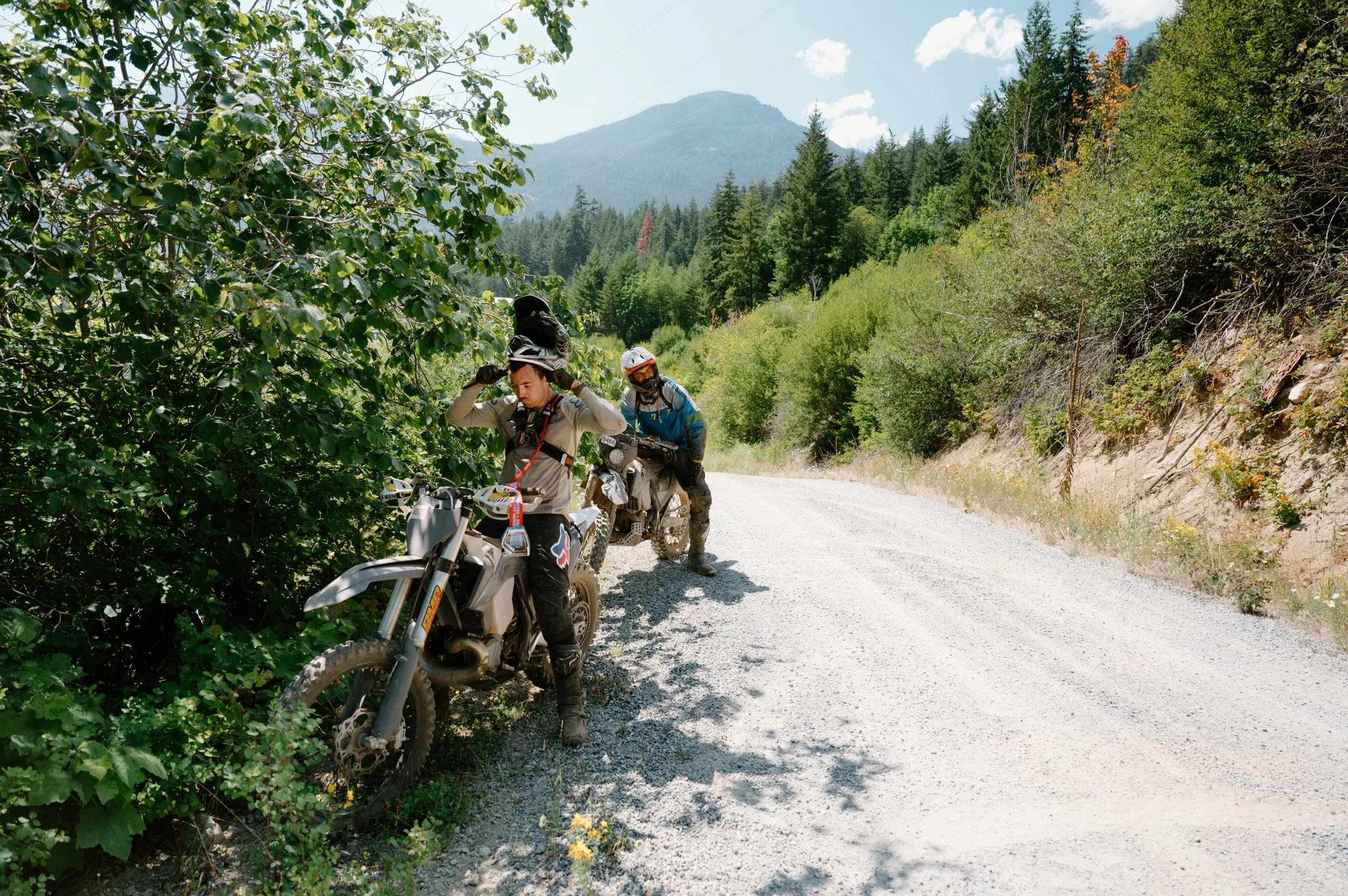 Two dirt bike riders sitting stationary at the side of a trail in BC, preparing to ride