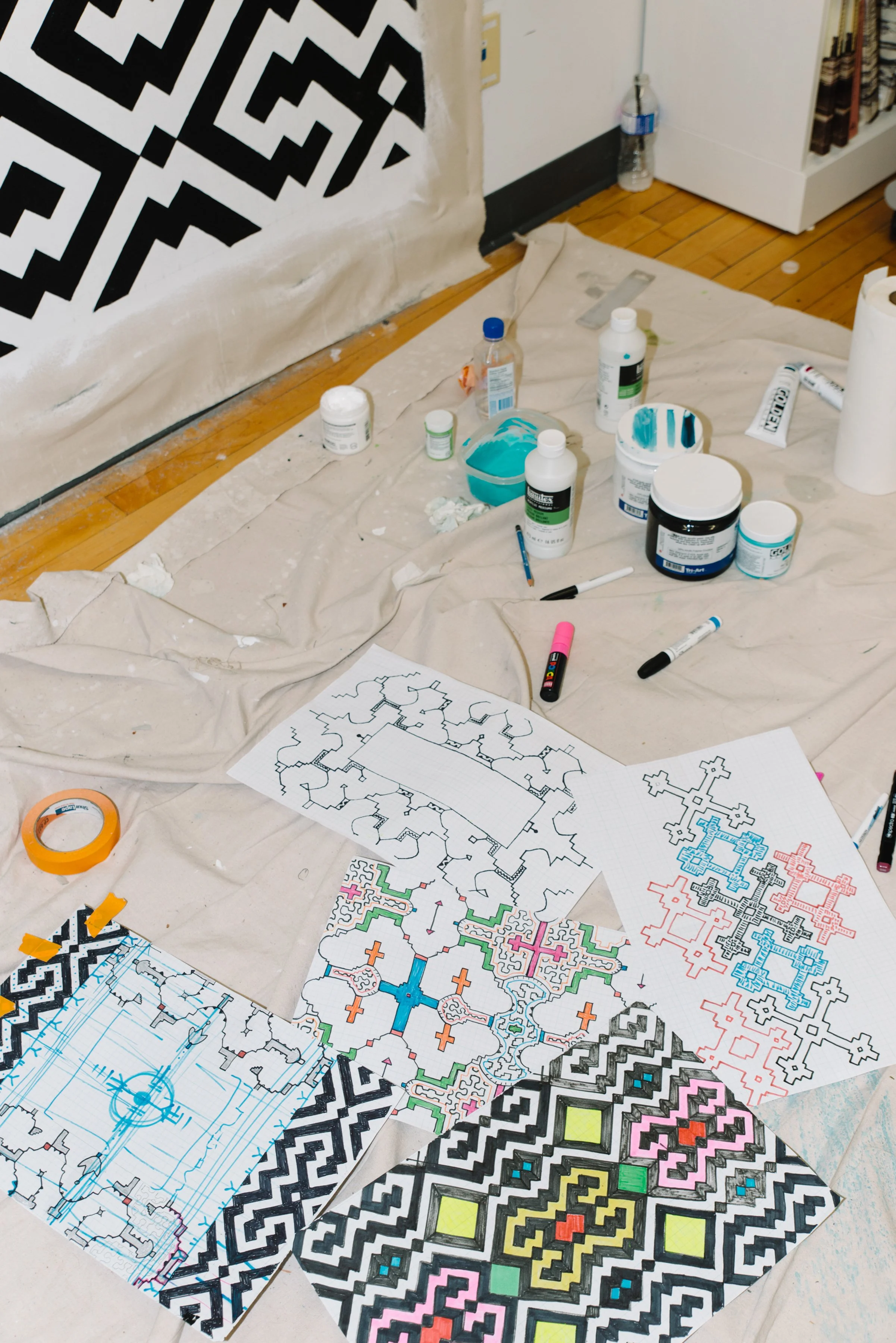 Detail photo of painting materials and rough draft sketches on the ground during the creation of the Paisajes de Nosotros mural at TMU
