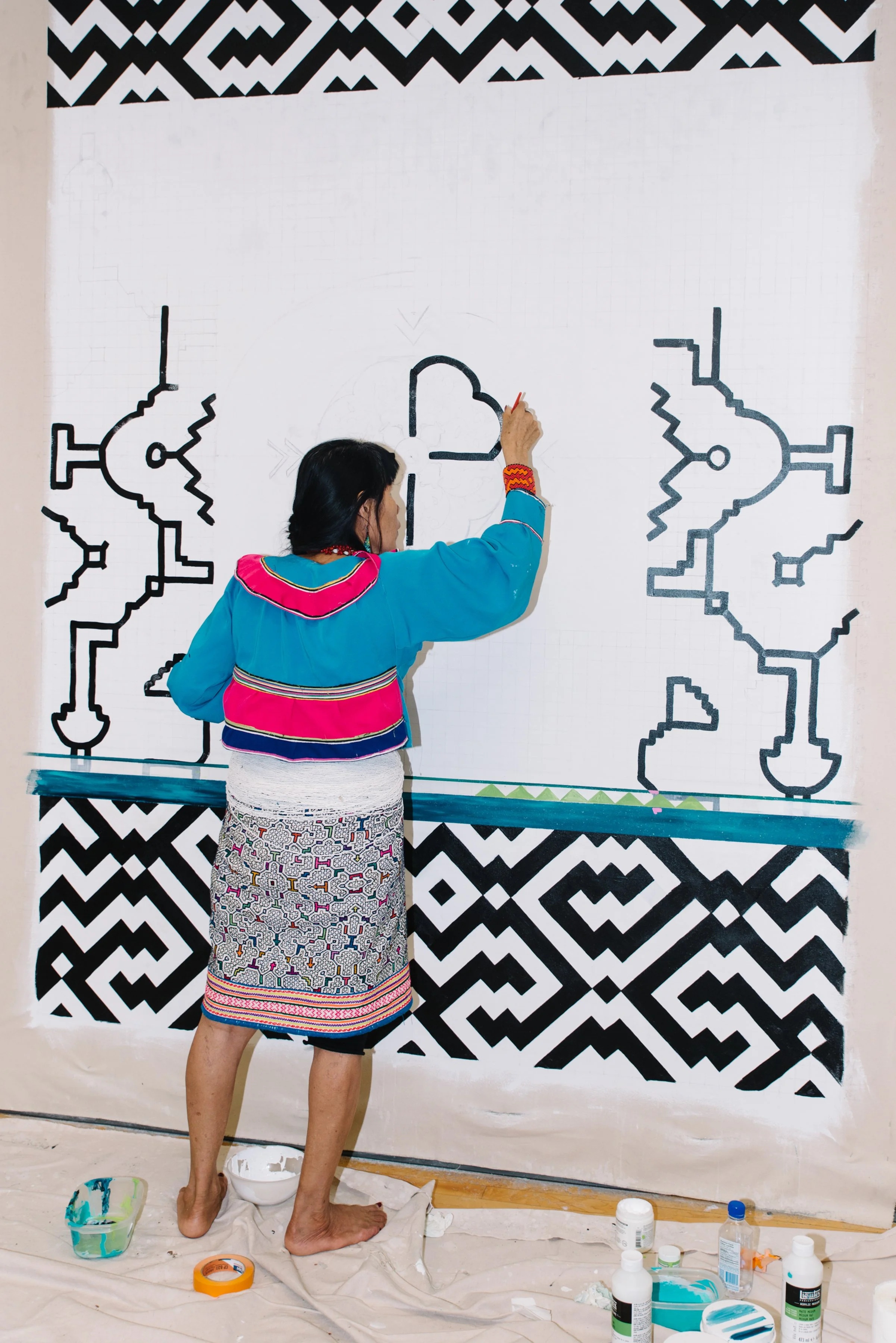 Wide documentary portrait of Olinda Reshinjabe Silvano at work on the large scale Arctic/Amazon public mural at TMU