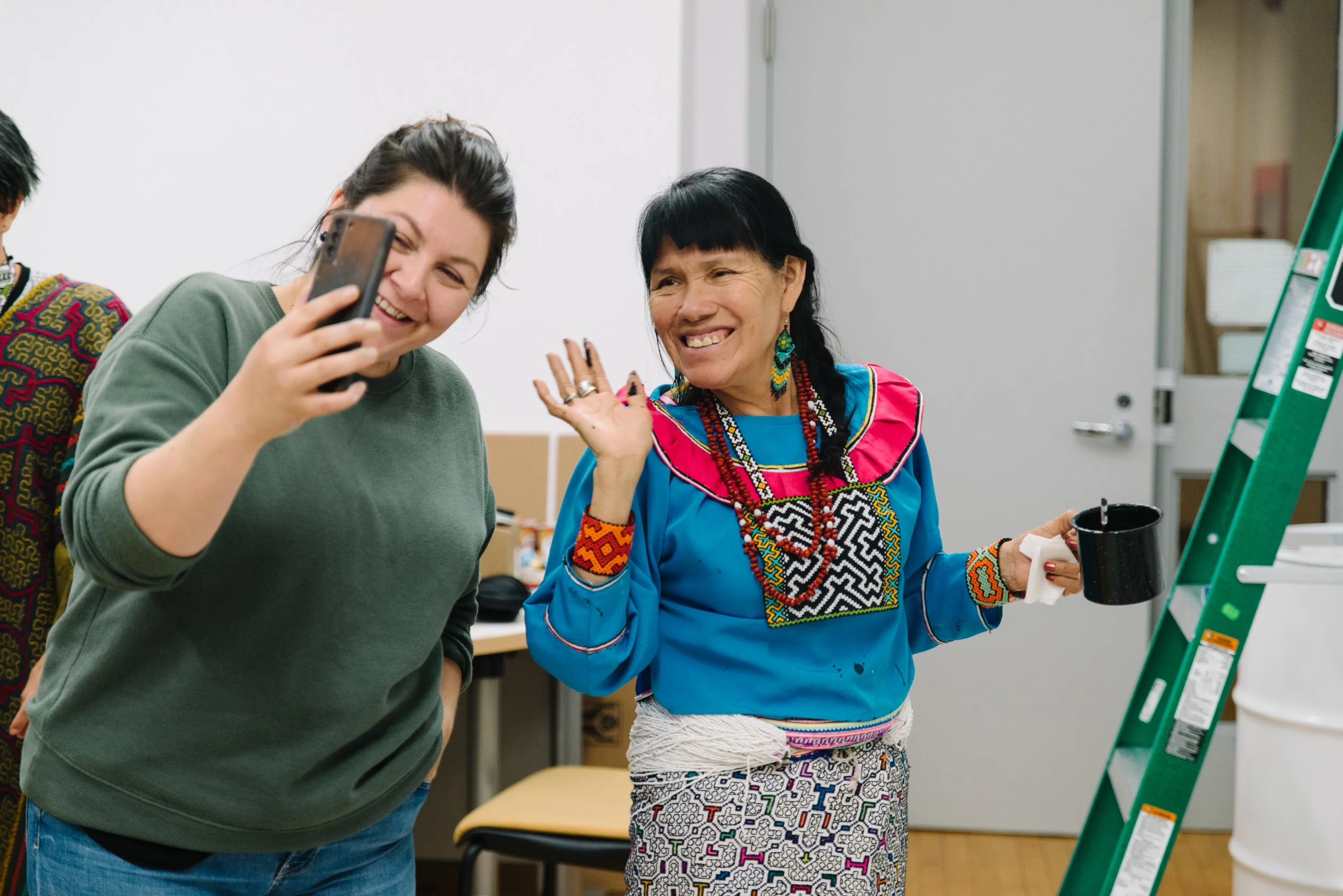 Candid documentary photo of Niap showing her phone to Olinda on a FaceTime call, both smiling and waving during the Arctic/Amazon mural collaboration