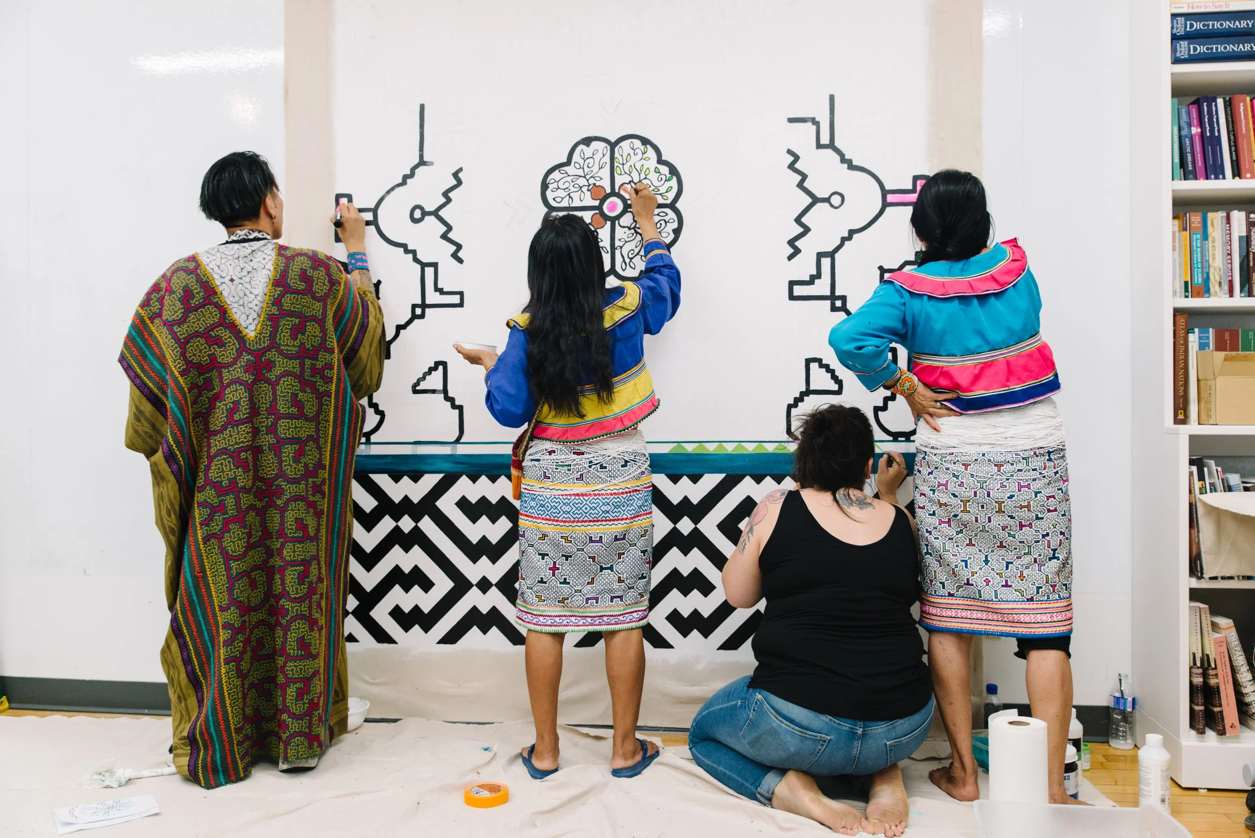 Documentary photo of Indigenous artists working together on the Paisajes de Nosotros mural at Toronto Metropolitan University, shot straight on with their backs to the camera