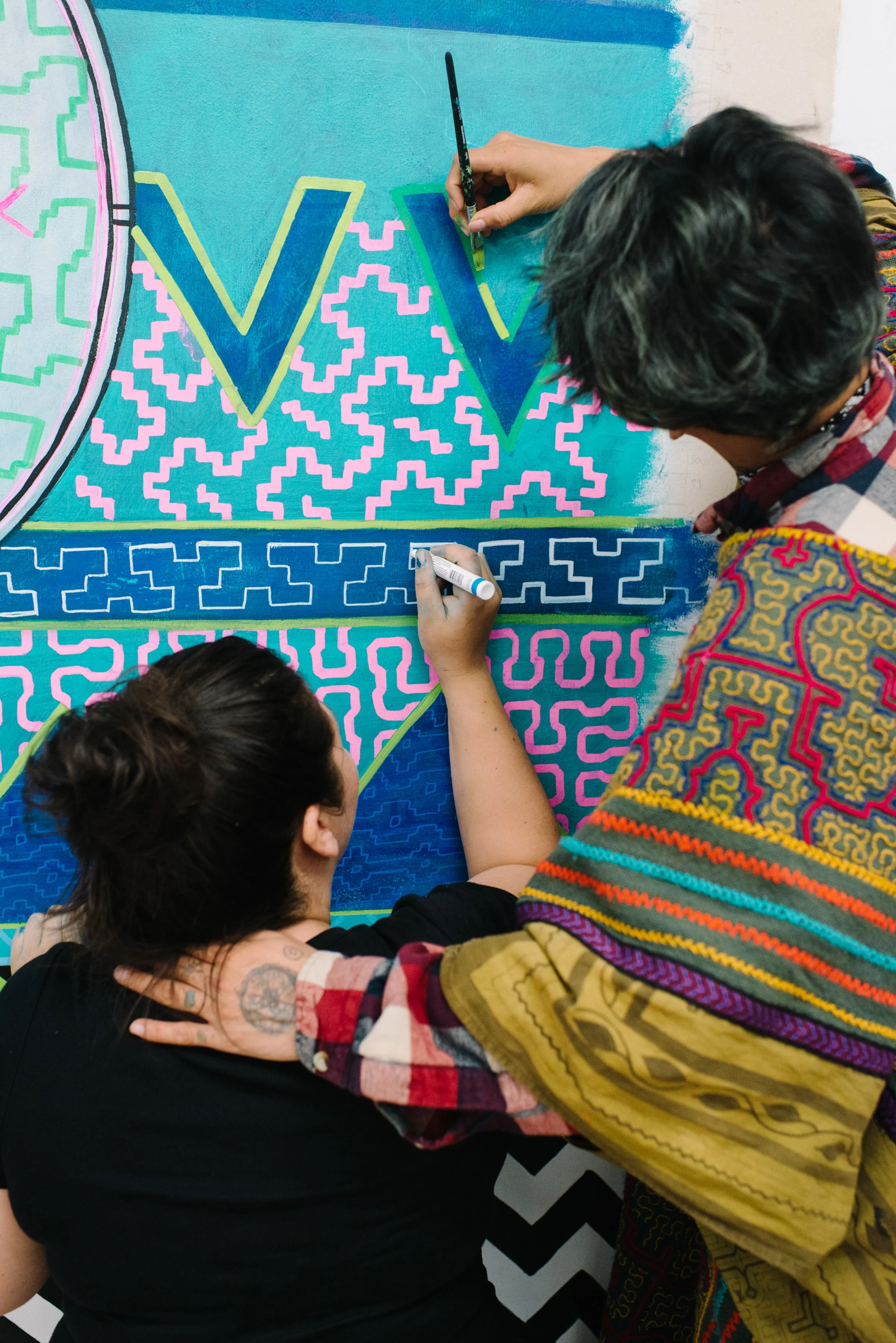 Portrait of Niap working alongside a collaborator, both painting the Arctic/Amazon mural at Toronto Metropolitan University