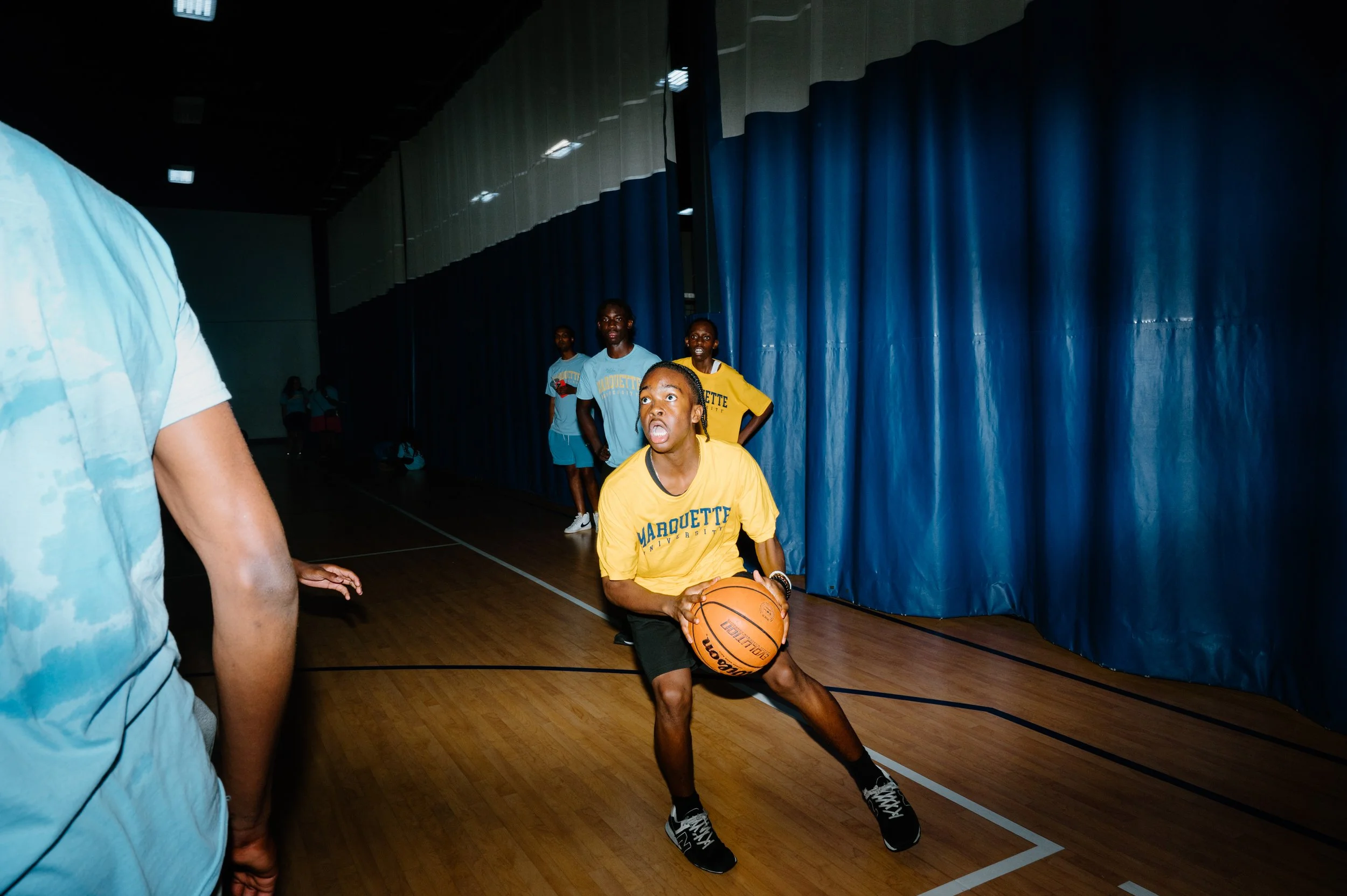 Hard flash editorial photo of a Marquette basketball player driving toward the net for a layup during practice