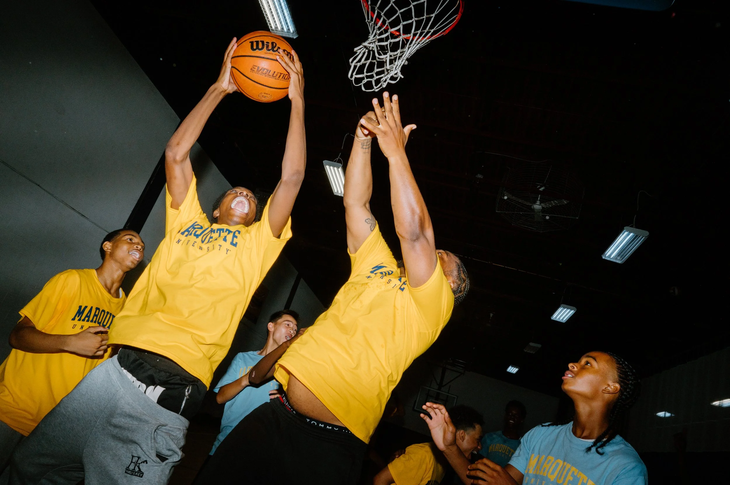 Low angle flash photo of a player going for a layup with Junior Cadougan contesting the shot at Marquette University