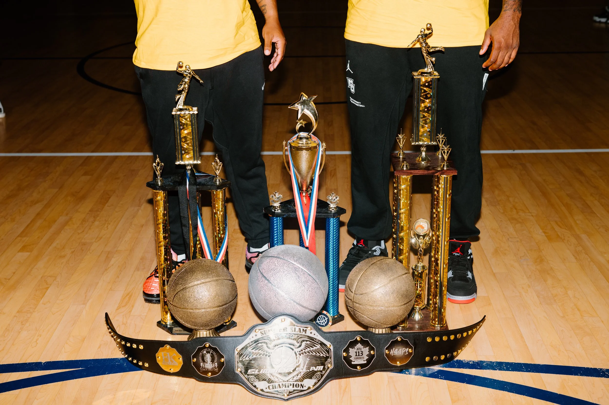 Portrait of Junior Cadougan and his co-head coach standing together behind trophies at Marquette University