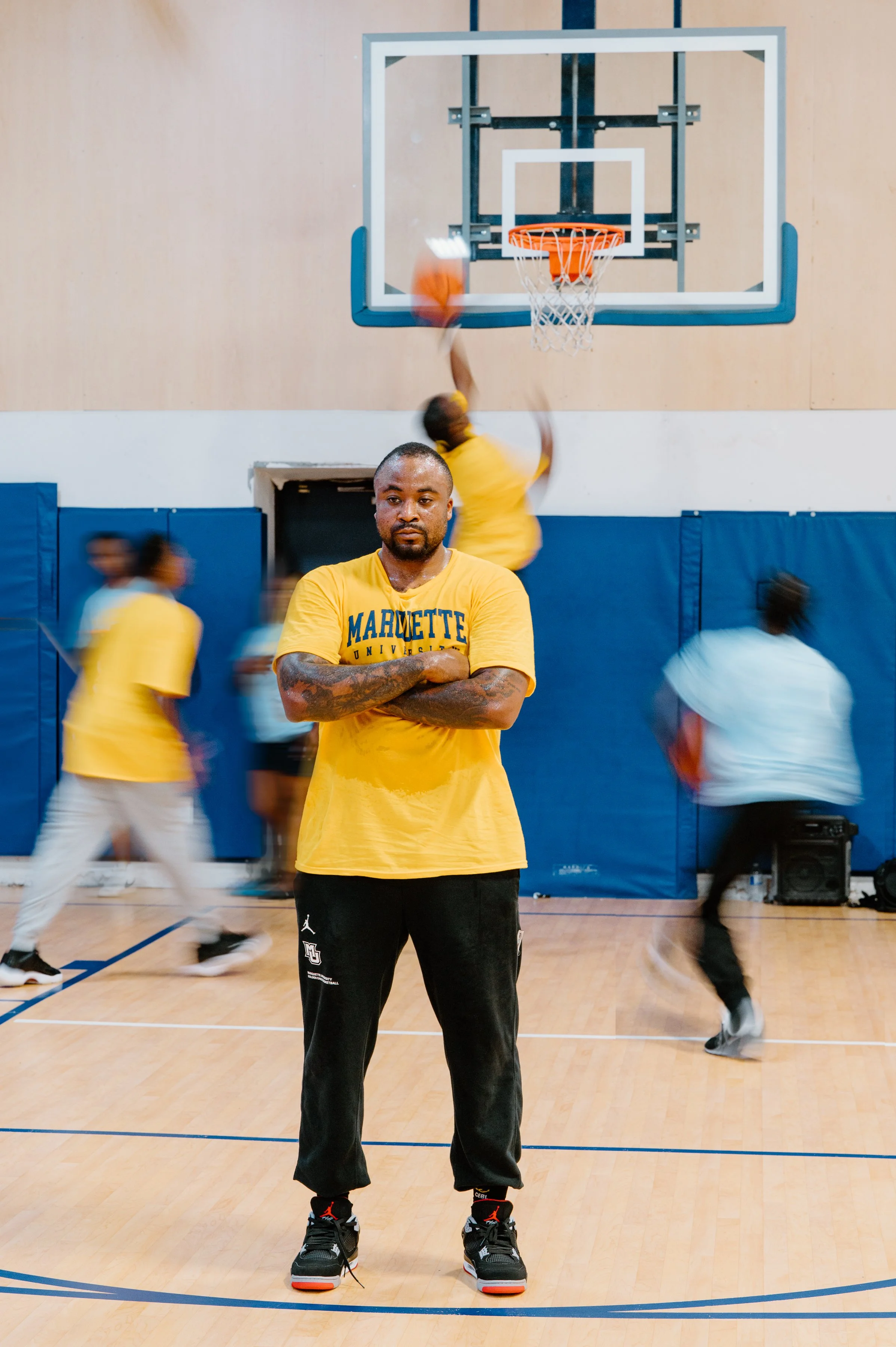 Editorial portrait of Junior Cadougan standing sharp and in focus while teammates move in motion blur around him during practice