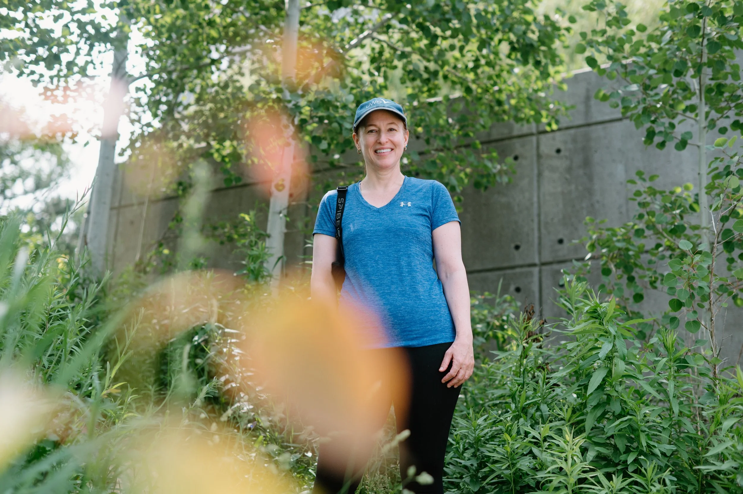 Lifestyle headshot of a woman in athletic wear standing outside amongst some green foliage.