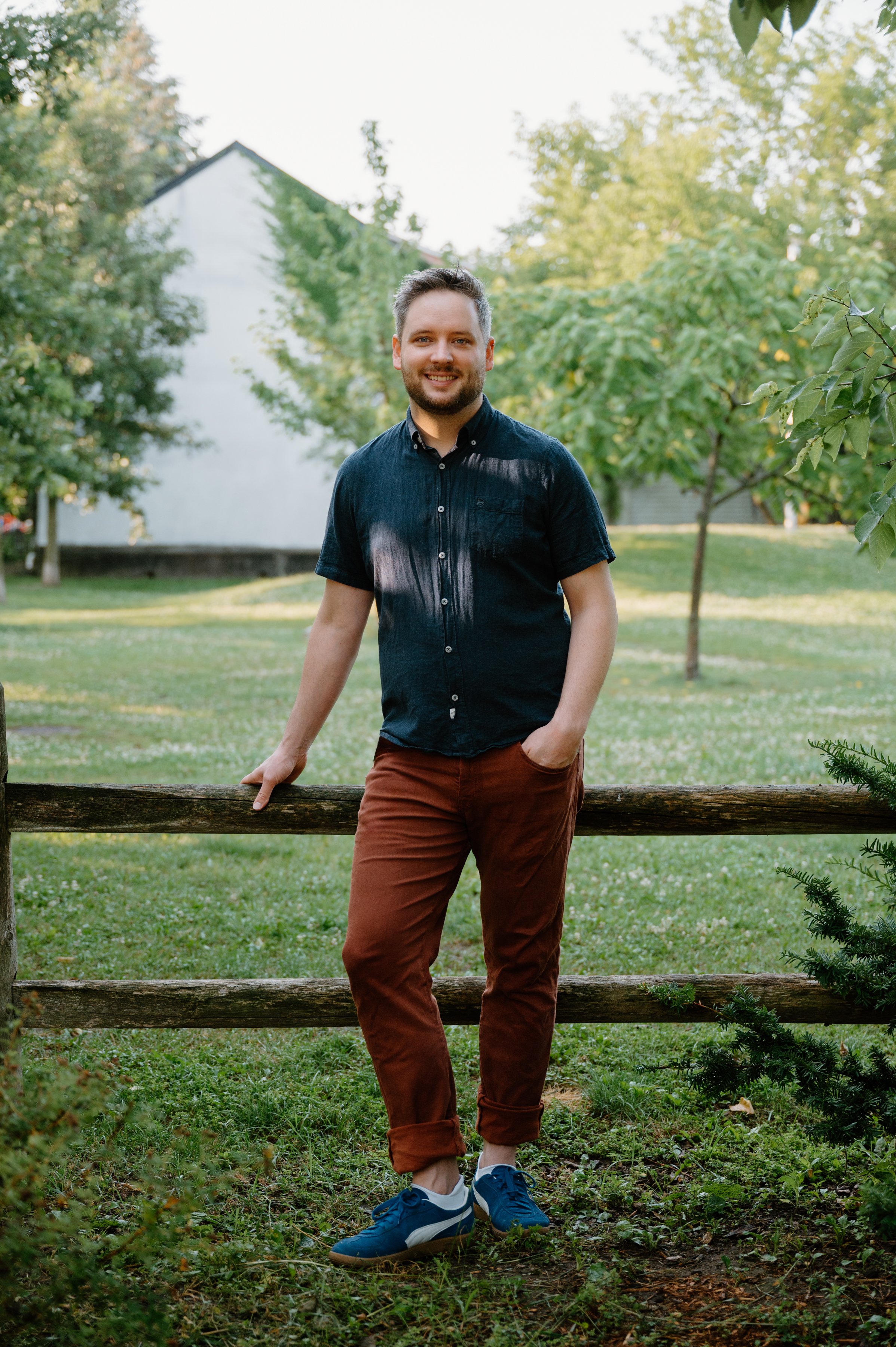 Candid lifestyle portrait of a man leaning against a fence at Wychwood Barns in Toronto, smiling at the camera