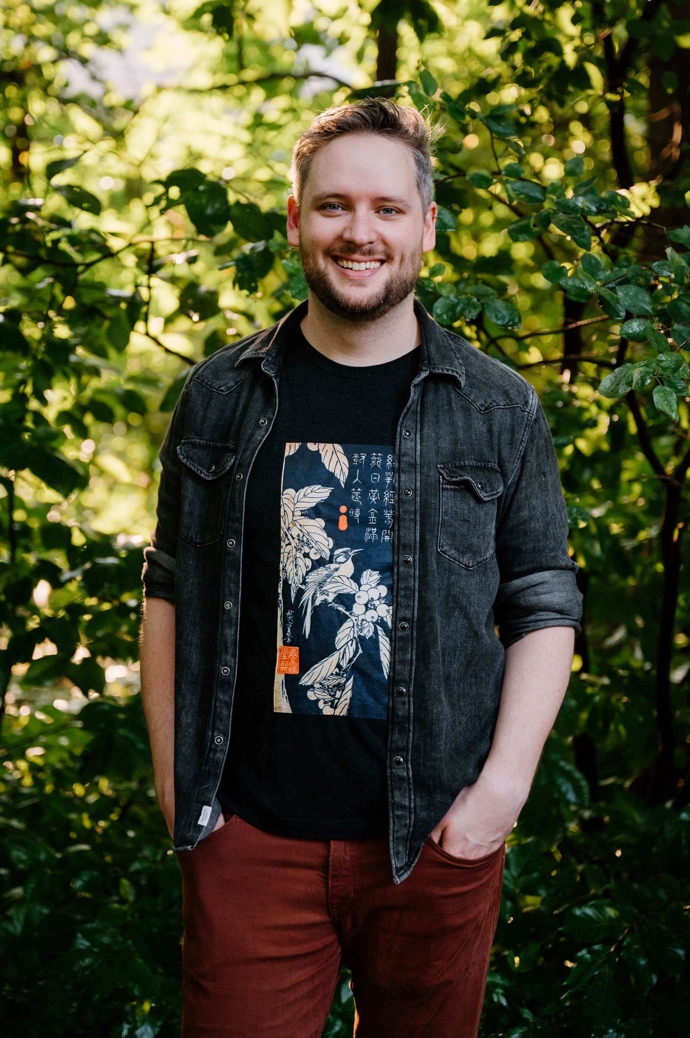 Outdoor lifestyle portrait of a man standing in front of green foliage with warm sunlight shining behind him at Wychwood Barns, Toronto