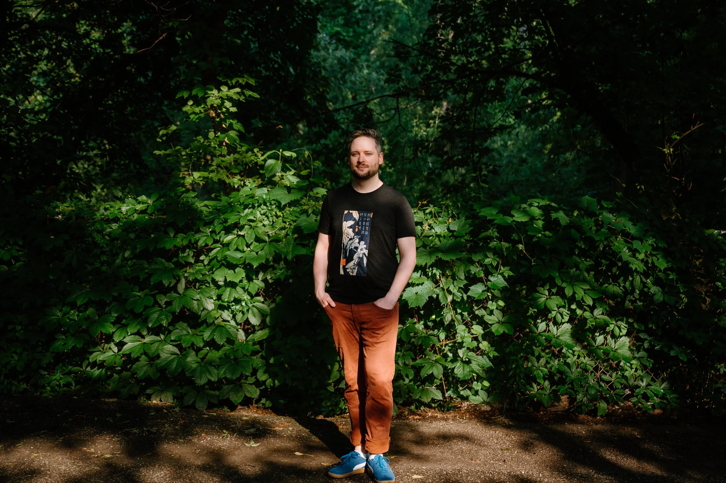Dramatic lifestyle portrait of a man standing in a sliver of natural light against shadowed greenery at Wychwood Barns in Toronto