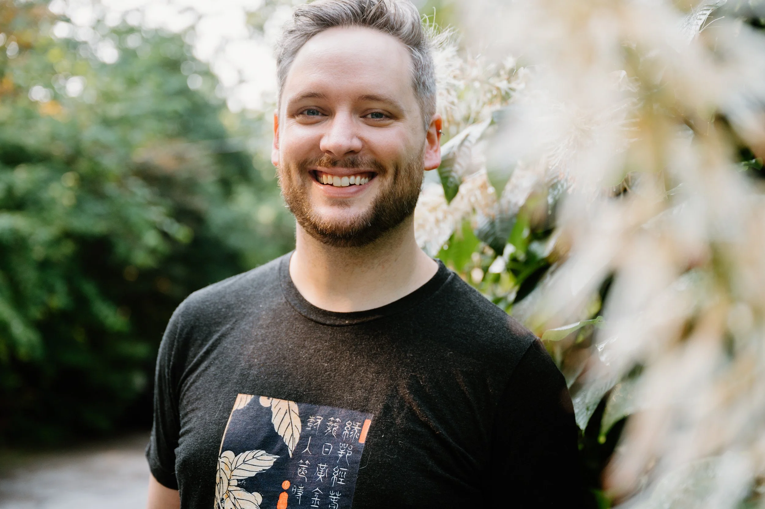 Lifestyle portrait of a man smiling at the camera with soft foreground foliage creating a warm glow in Toronto