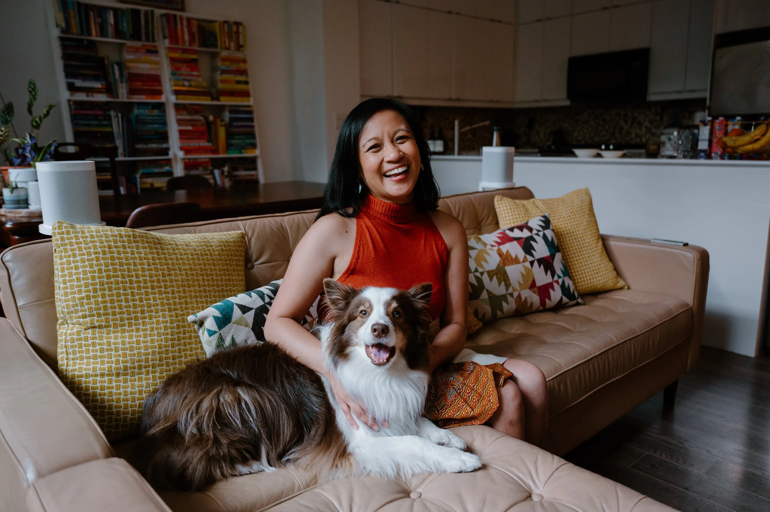 Warm lifestyle author portrait of Jennilee Austria-Bonifacio seated on her couch with her dog at her home near Trinity Bellwoods, Toronto