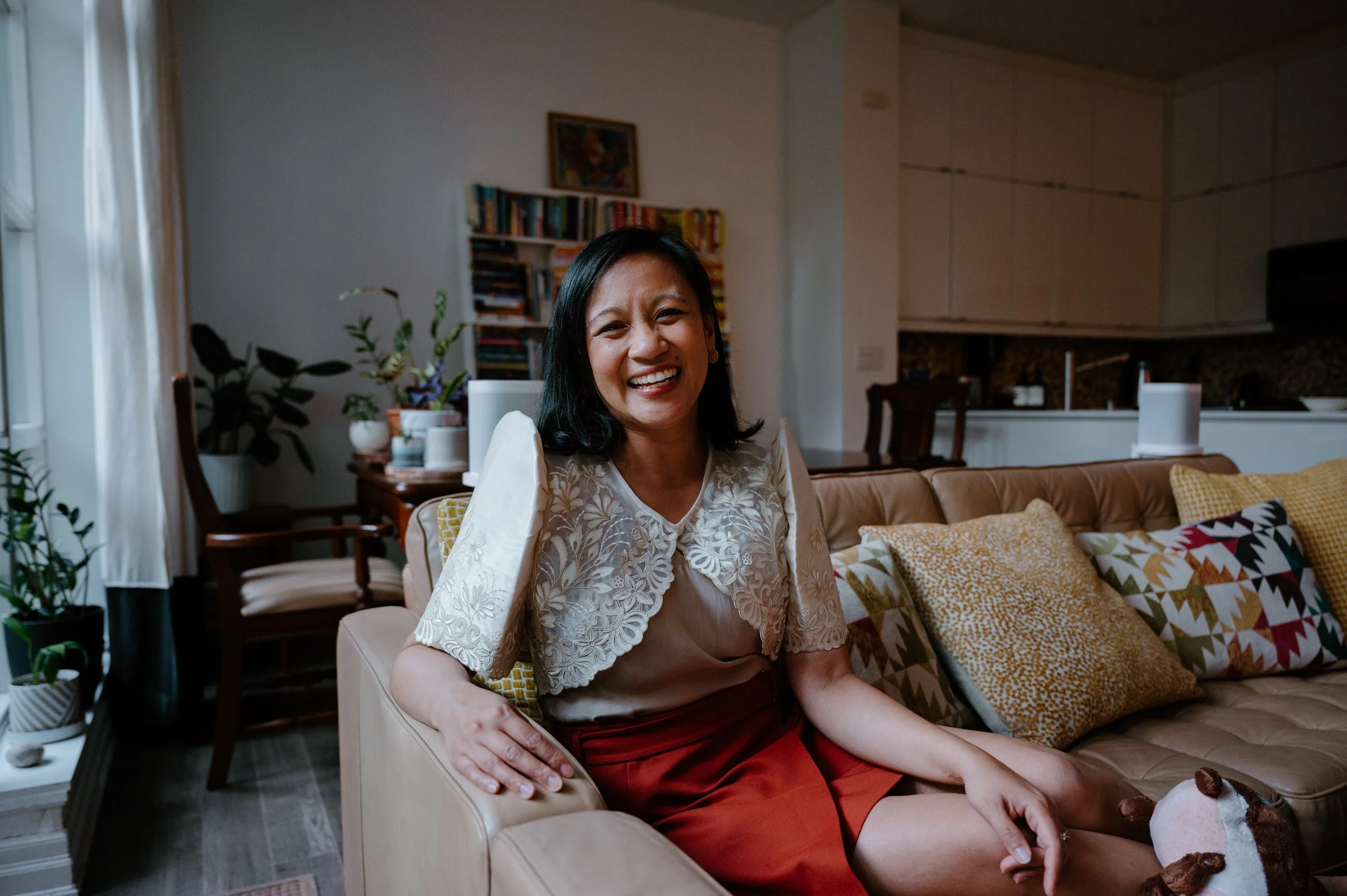Candid lifestyle portrait of author Jennilee Austria-Bonifacio on her couch wearing a Filipiniana terno, photographed at home in Toronto