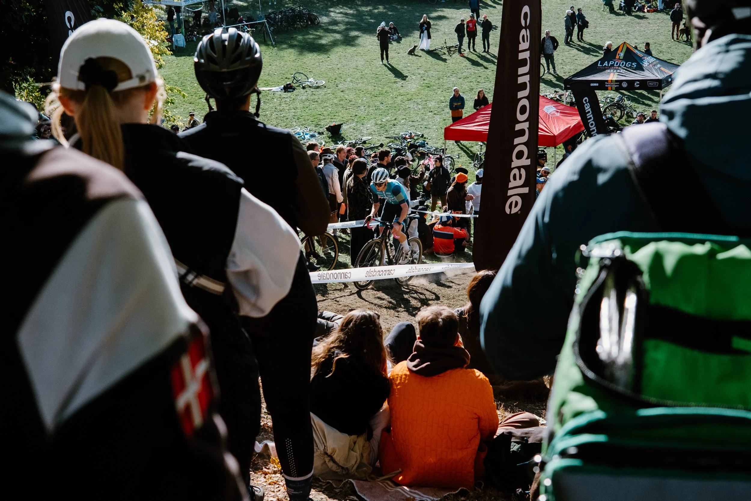 Documentary photo of cyclocross riders pushing uphill at Christie Cross, photographed through the spectator crowd lining the course