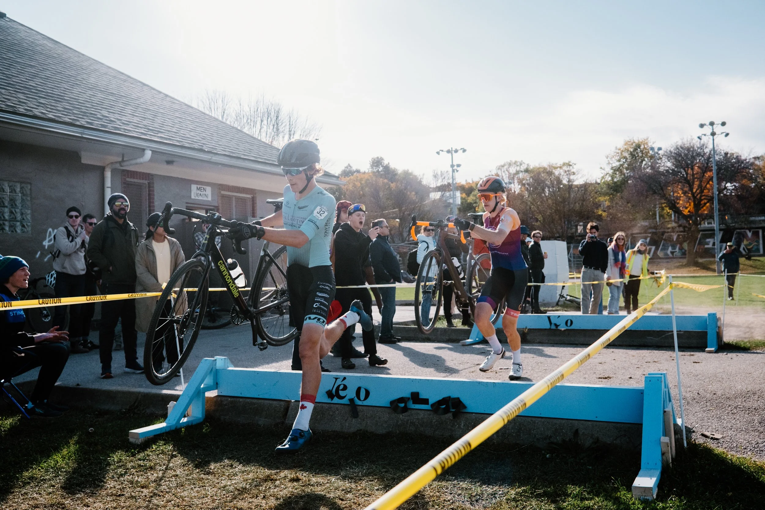 Cyclocross riders launching over a course obstacle at Christie Cross in Toronto, captured mid-air in documentary style