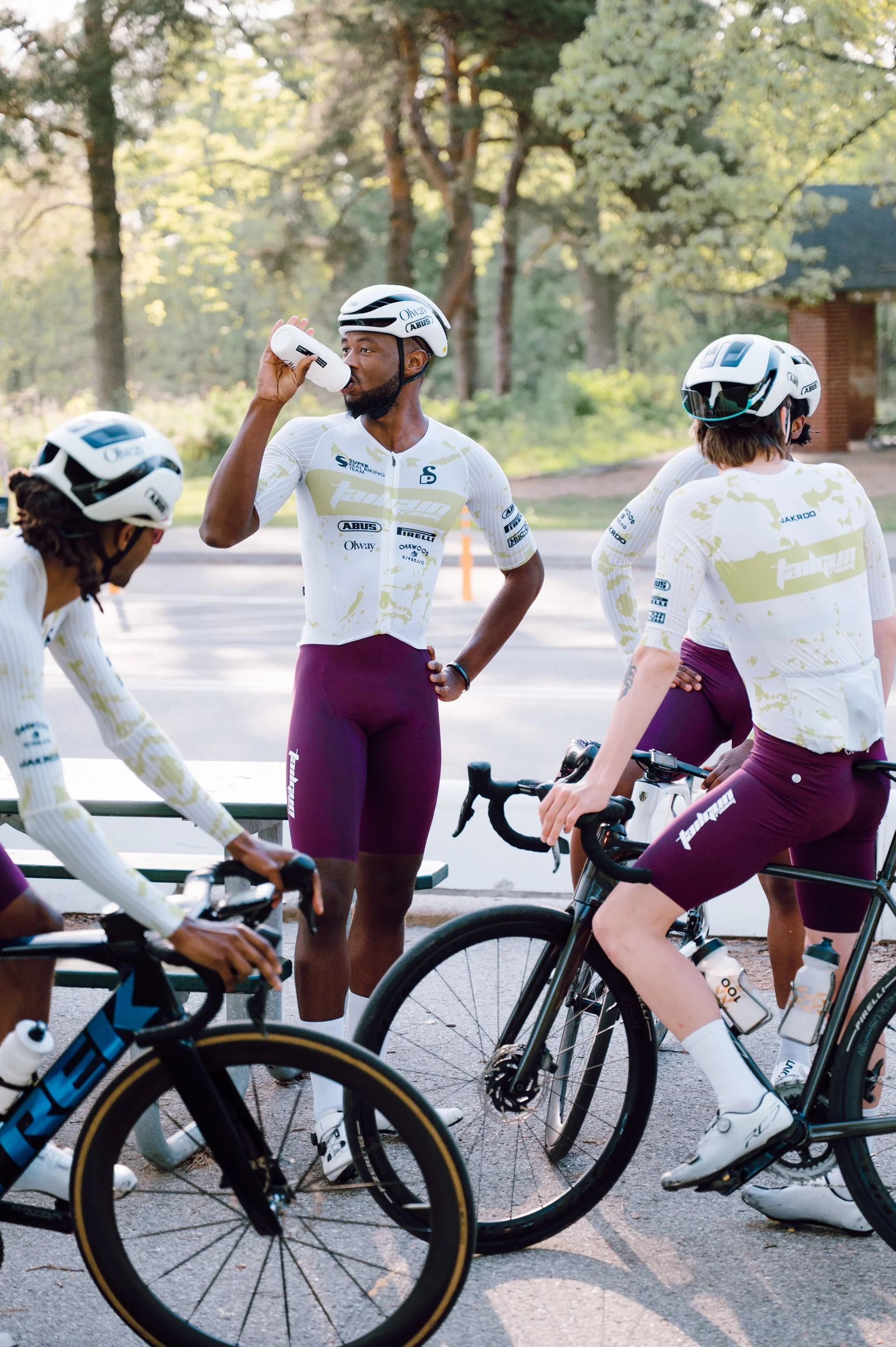 Candid lifestyle photo of a cycling team taking a break at High Park, one rider drinking water while others prepare to ride