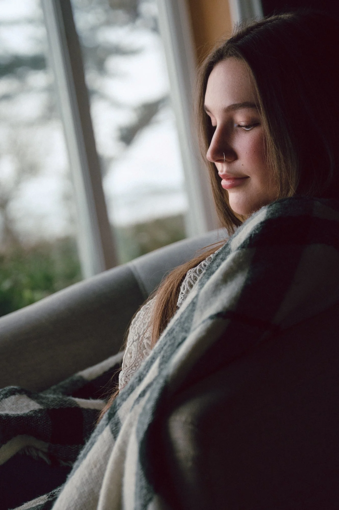 Serene close-up editorial portrait of a model seated at a cottage window in Sooke BC, looking downward in soft natural light