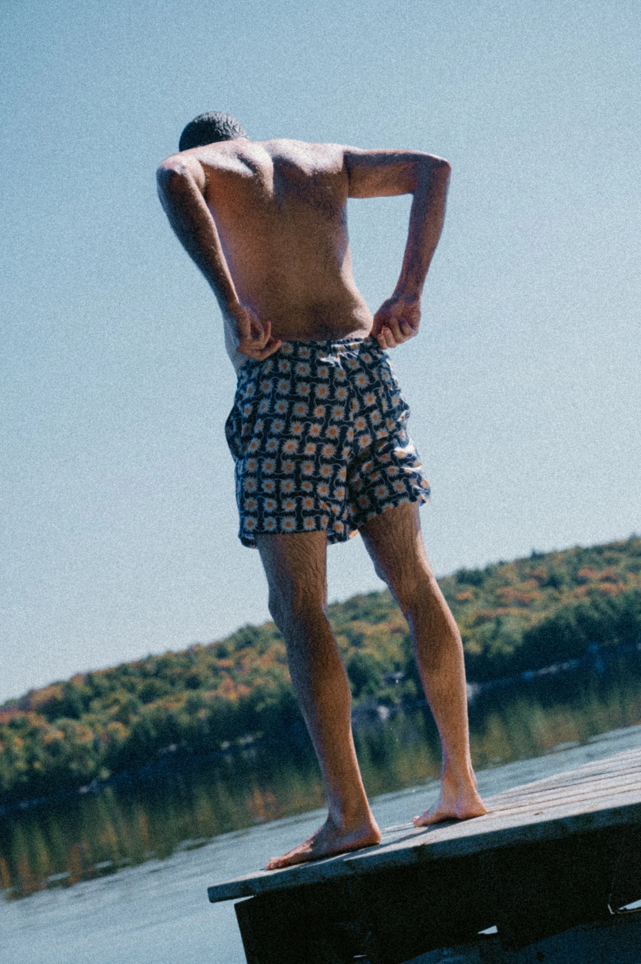 Lifestyle campaign photo of a person standing on a cottage dock wearing Bather swim trunks, back to the camera