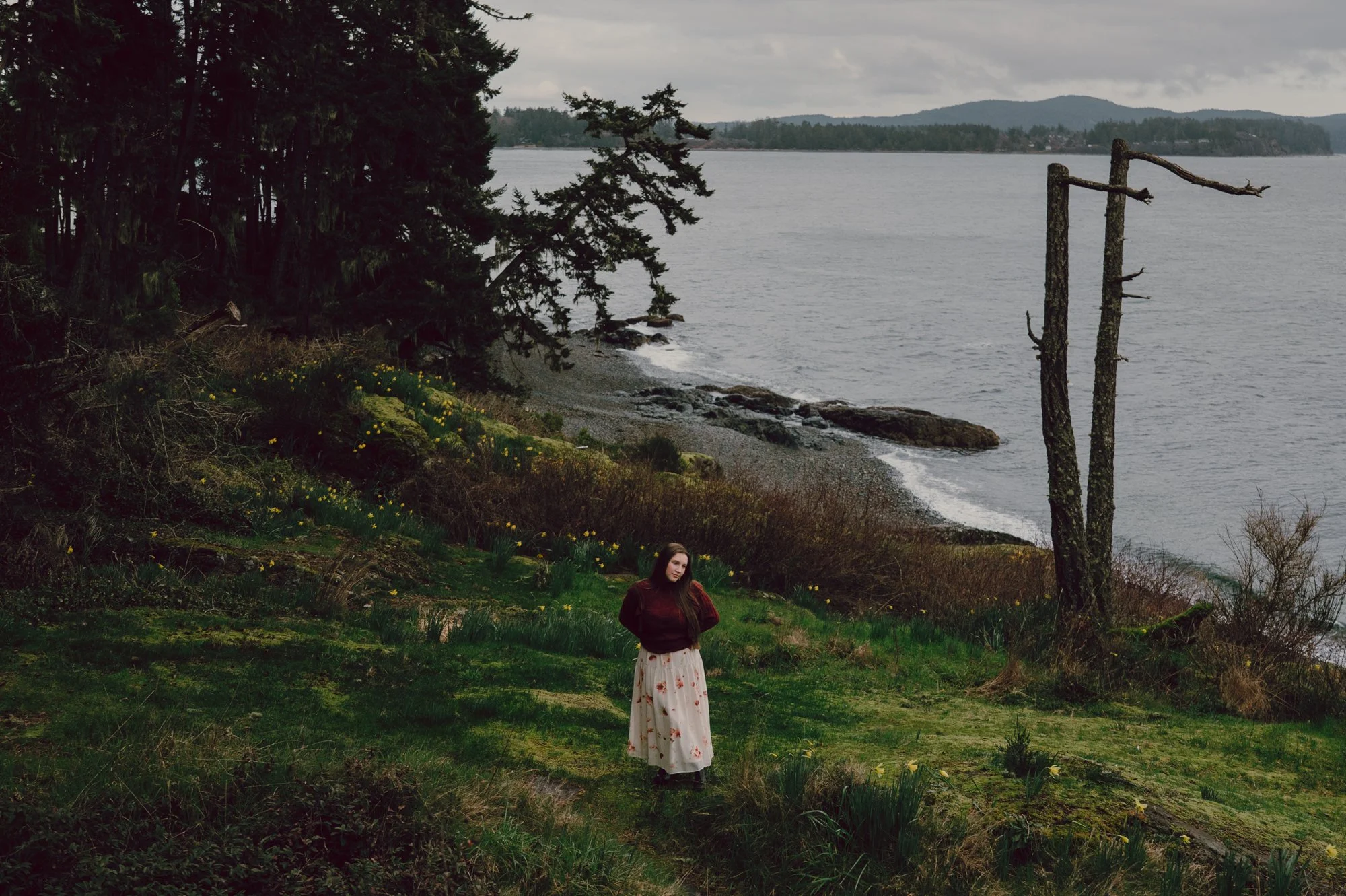 Lifestyle portrait of a model standing on a green hillside with the Pacific Ocean behind her in Sooke, BC
