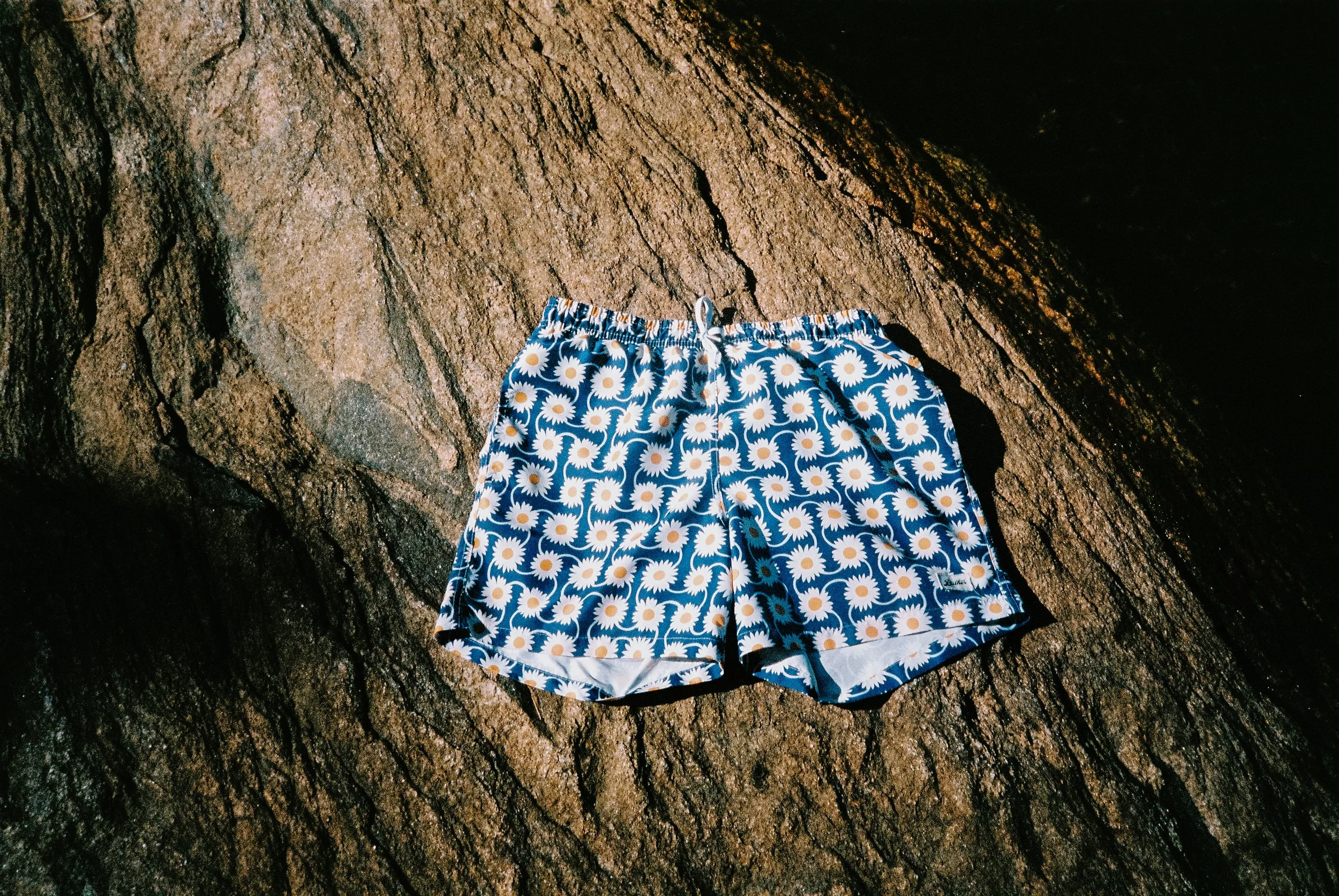 Product lifestyle photo of Bather swim trunks resting on a rock in dappled sunlight at a cottage