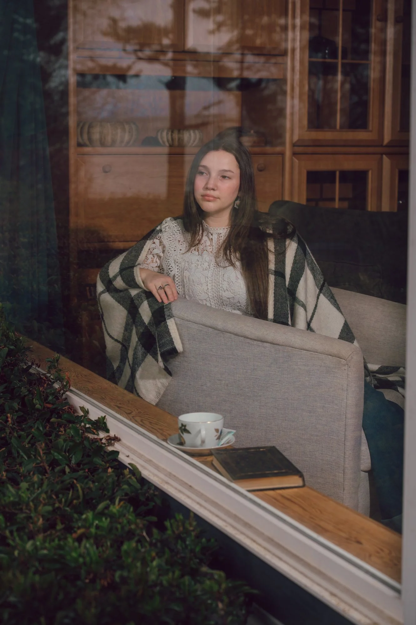 Editorial lifestyle photo of a model sitting inside an oceanfront cottage, captured from outside looking in through the window on Vancouver Island