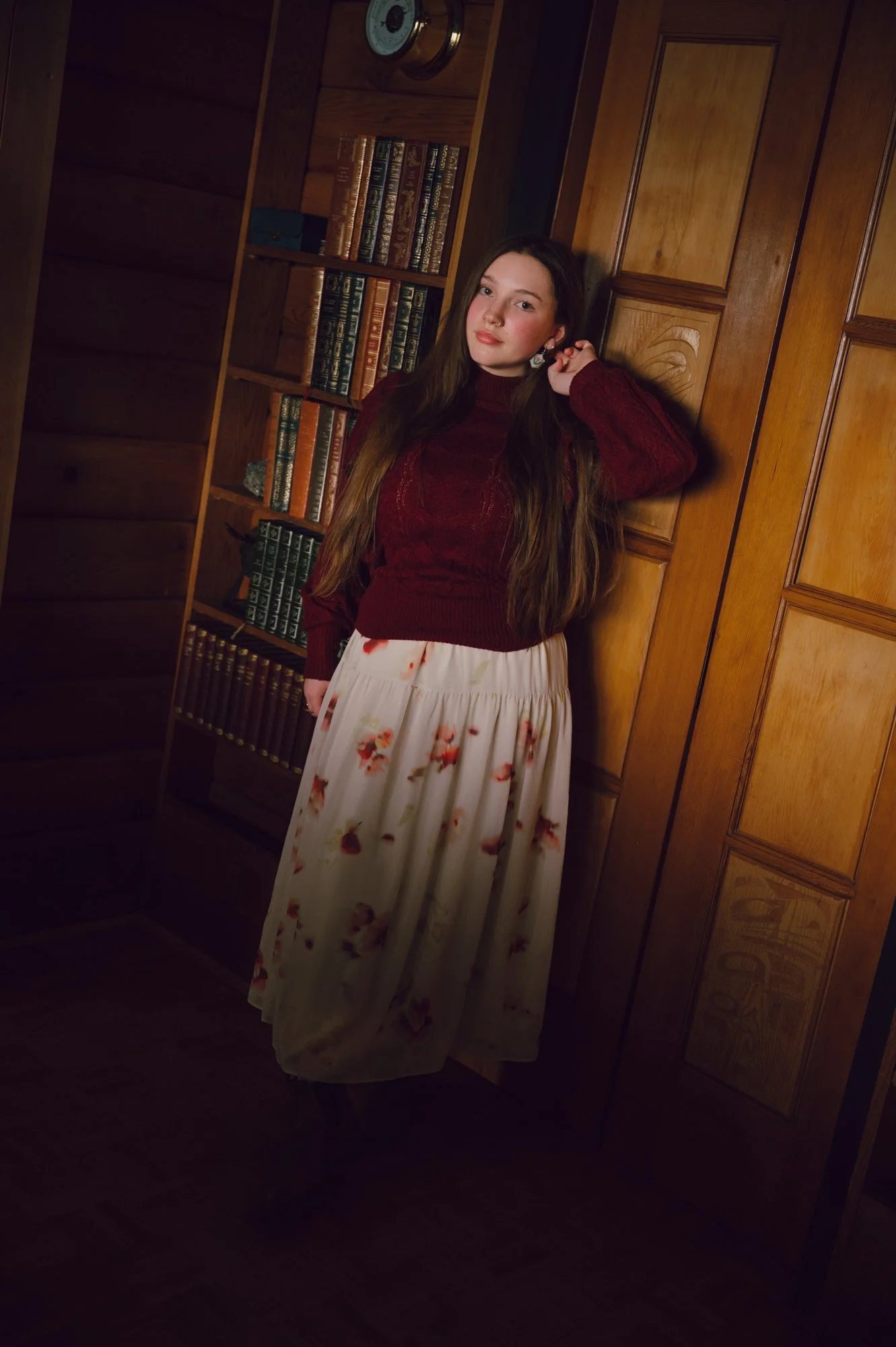 Lifestyle portrait of a model standing near a bookshelf inside a warm wooden pan abode cottage interior in Victoria BC