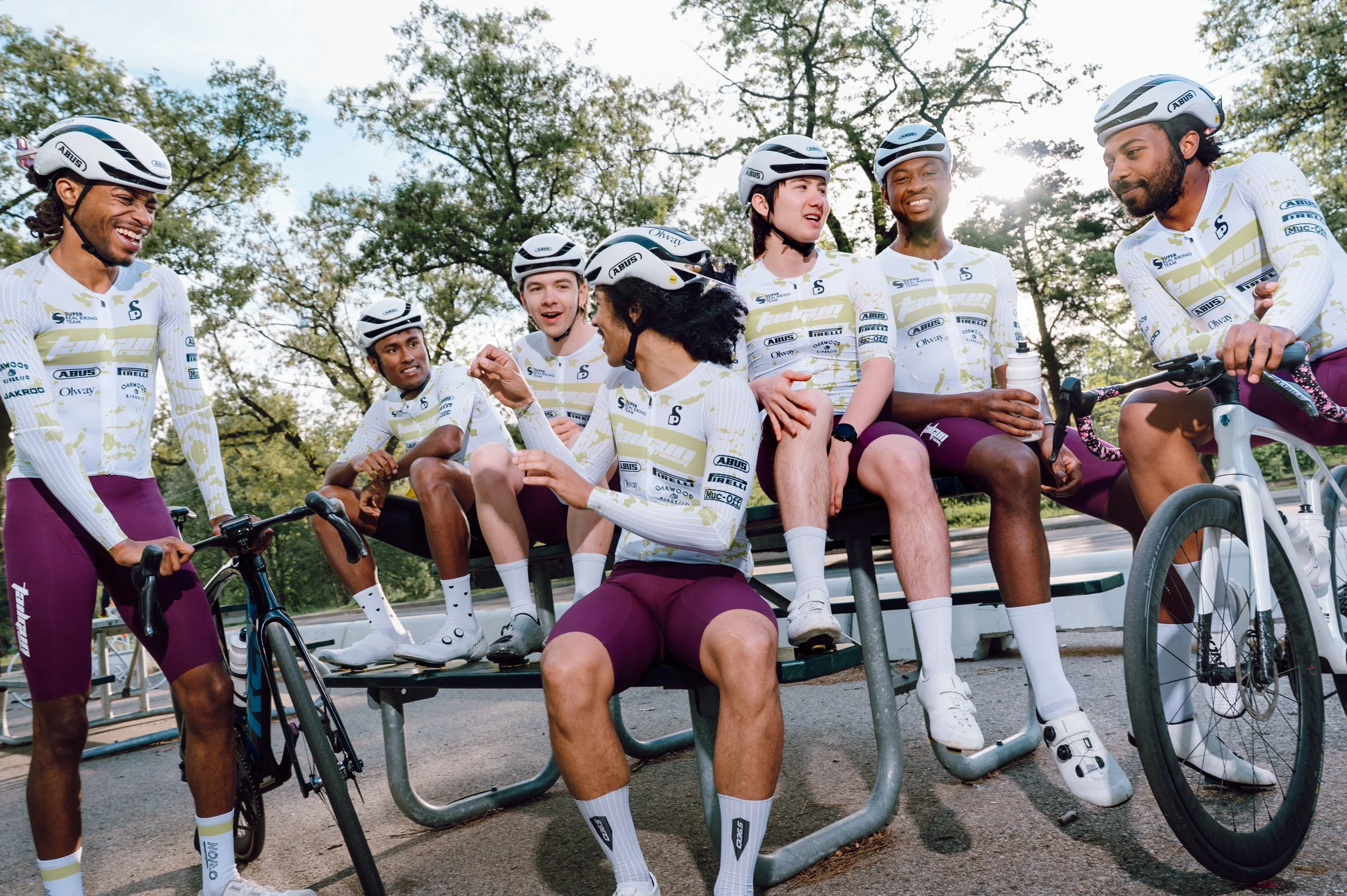 Candid photo of a road cycling team laughing and interacting at a picnic table during a break at High Park in Toronto