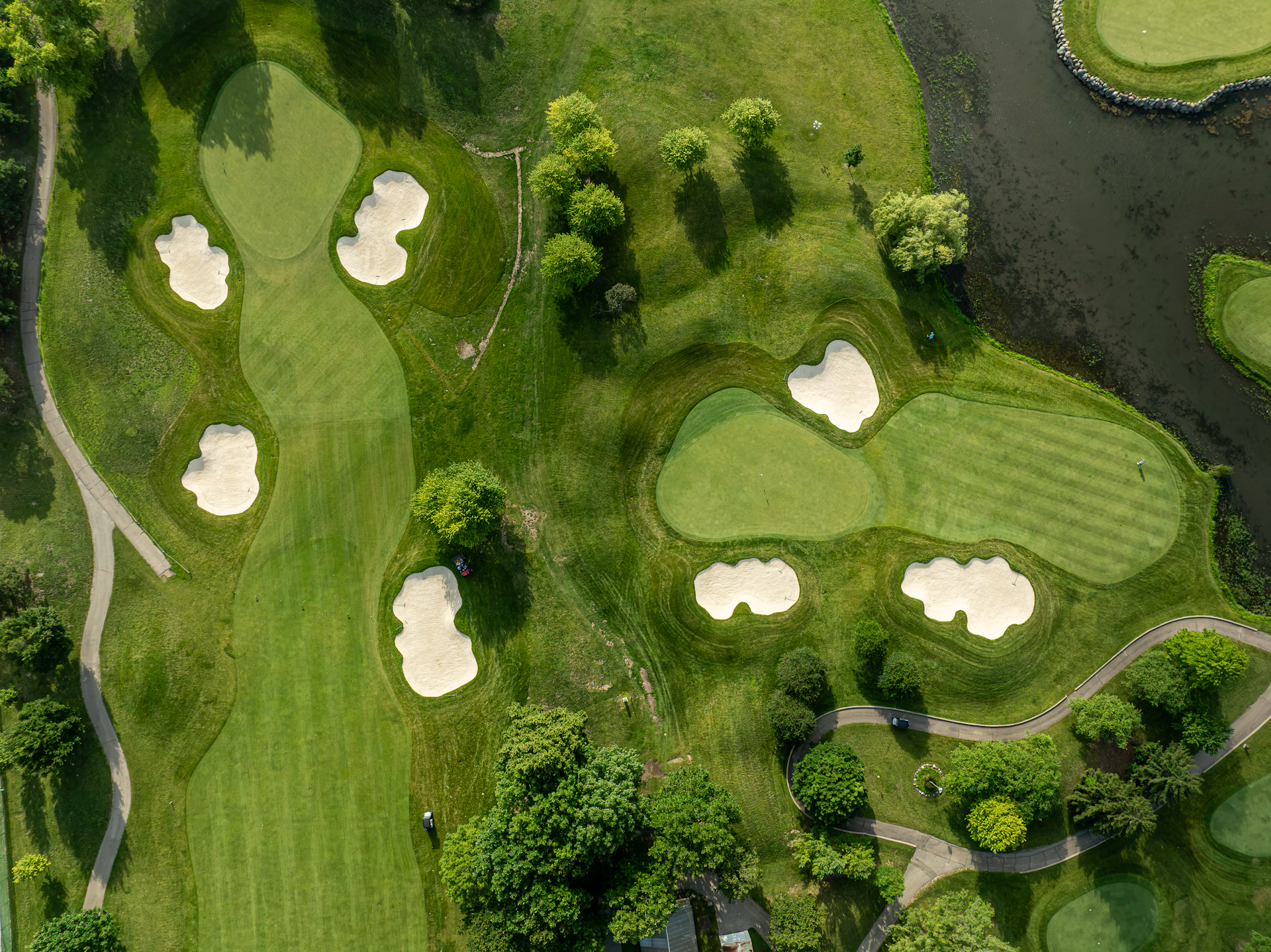 Aerial view of a golf course with multiple water hazards, sand bunkers, and green fairways surrounded by trees and a residential building in the background.