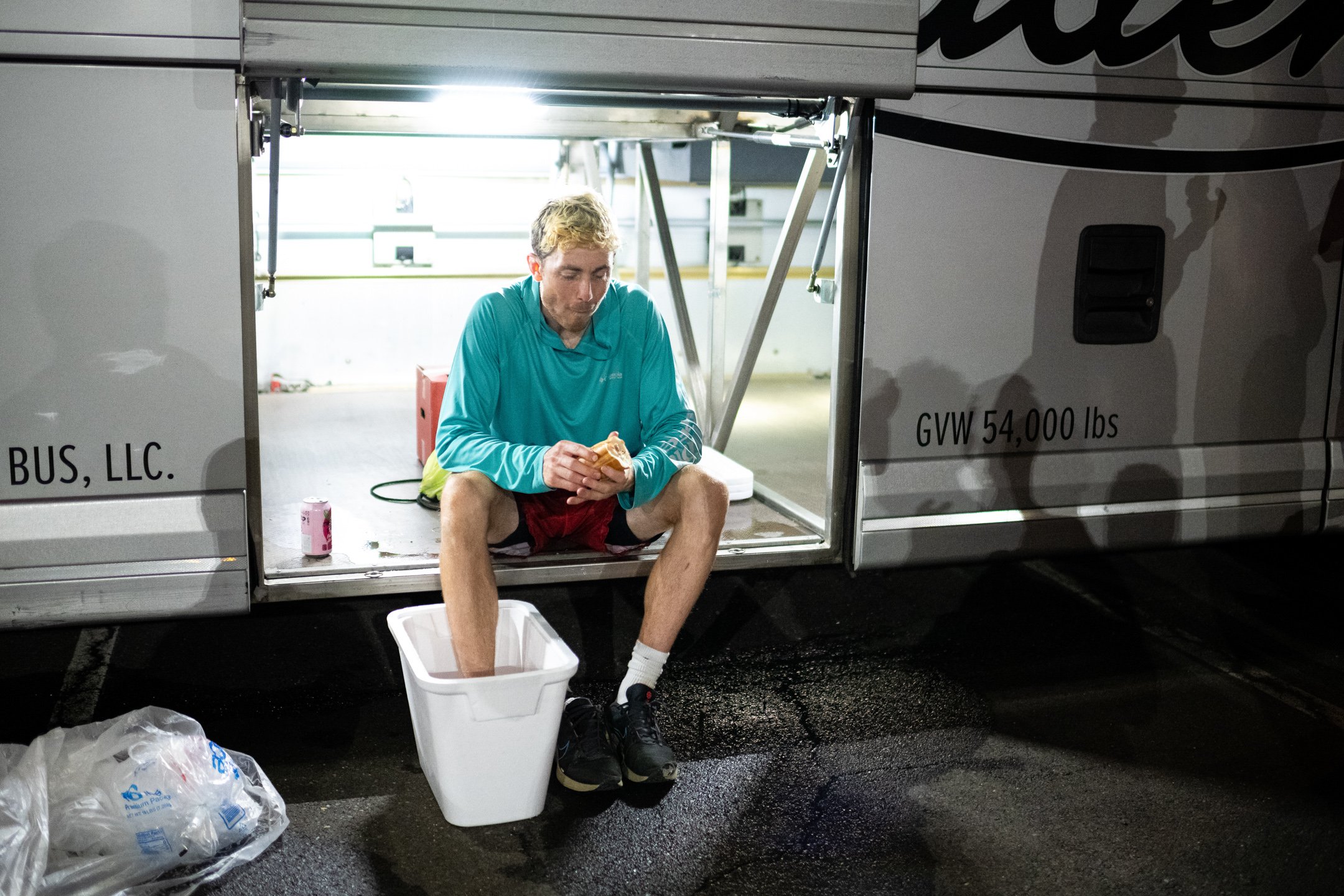  DC Breeze player Rowan McDonnell ices his foot in a styrofoam cooler and eats a sandwich while sitting in the luggage bay under the team bus, during a team meal after an away game against the Philadelphia Phoenix in the American Ultimate Disc League