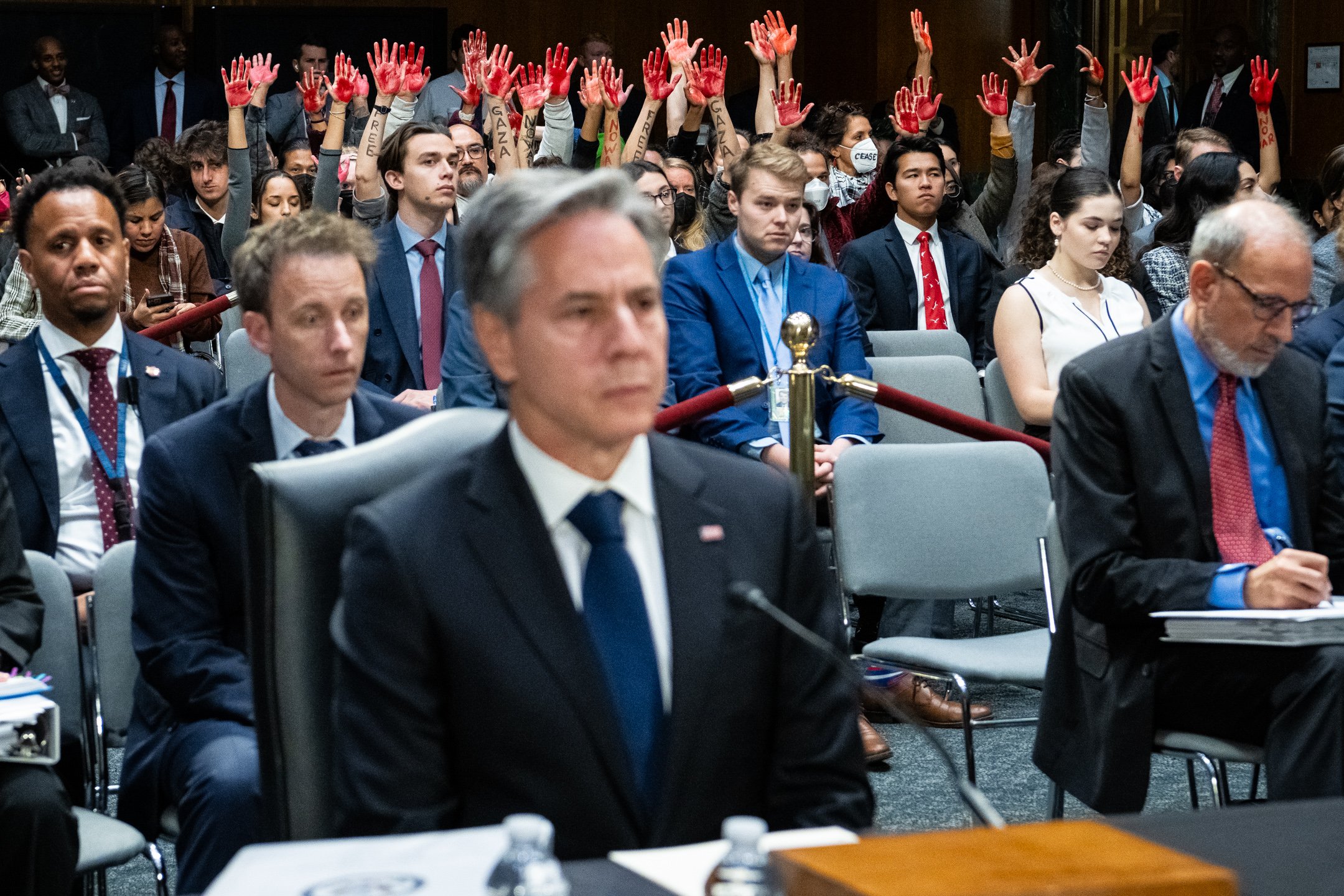  Protesters calling for a ceasefire in Gaza raise their hands painted to look like blood, in the audience behind Secretary of State Antony Blinken, during a Senate Appropriations Committee hearing to review President Biden’s request for emergency fun