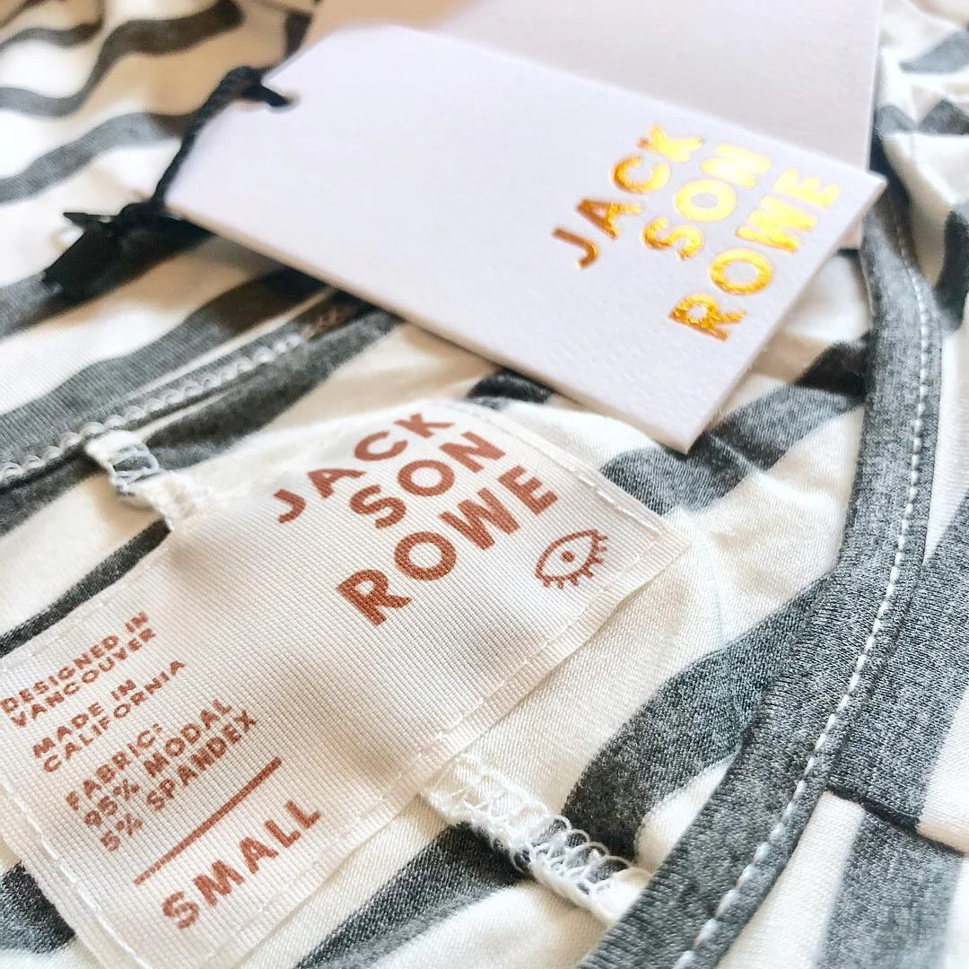 Close-up of a striped Jack by Jack Rouke clothing tag on a fabric with matching tags above. 