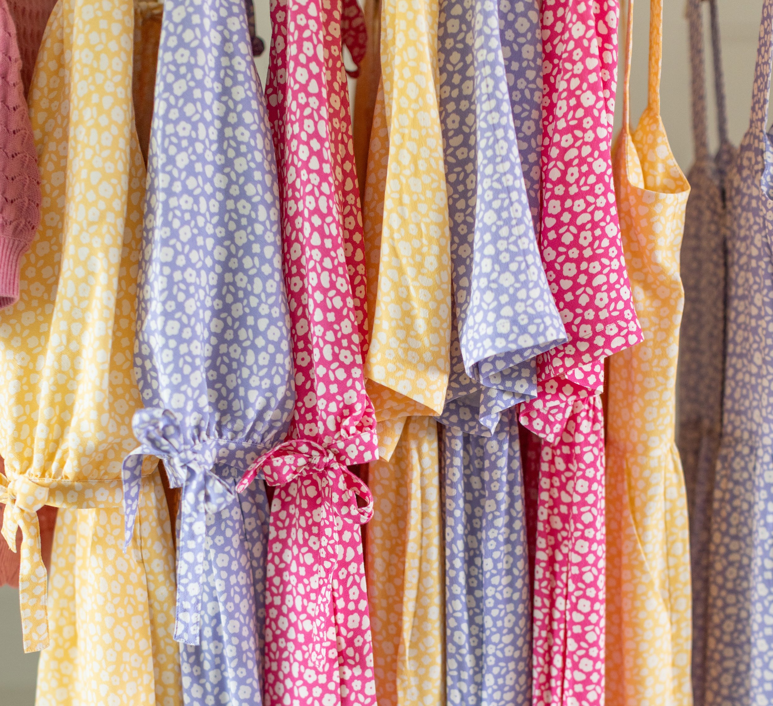 Colorful dresses with floral patterns hanging on a rack, featuring yellow, purple, pink, orange, and blue colors.