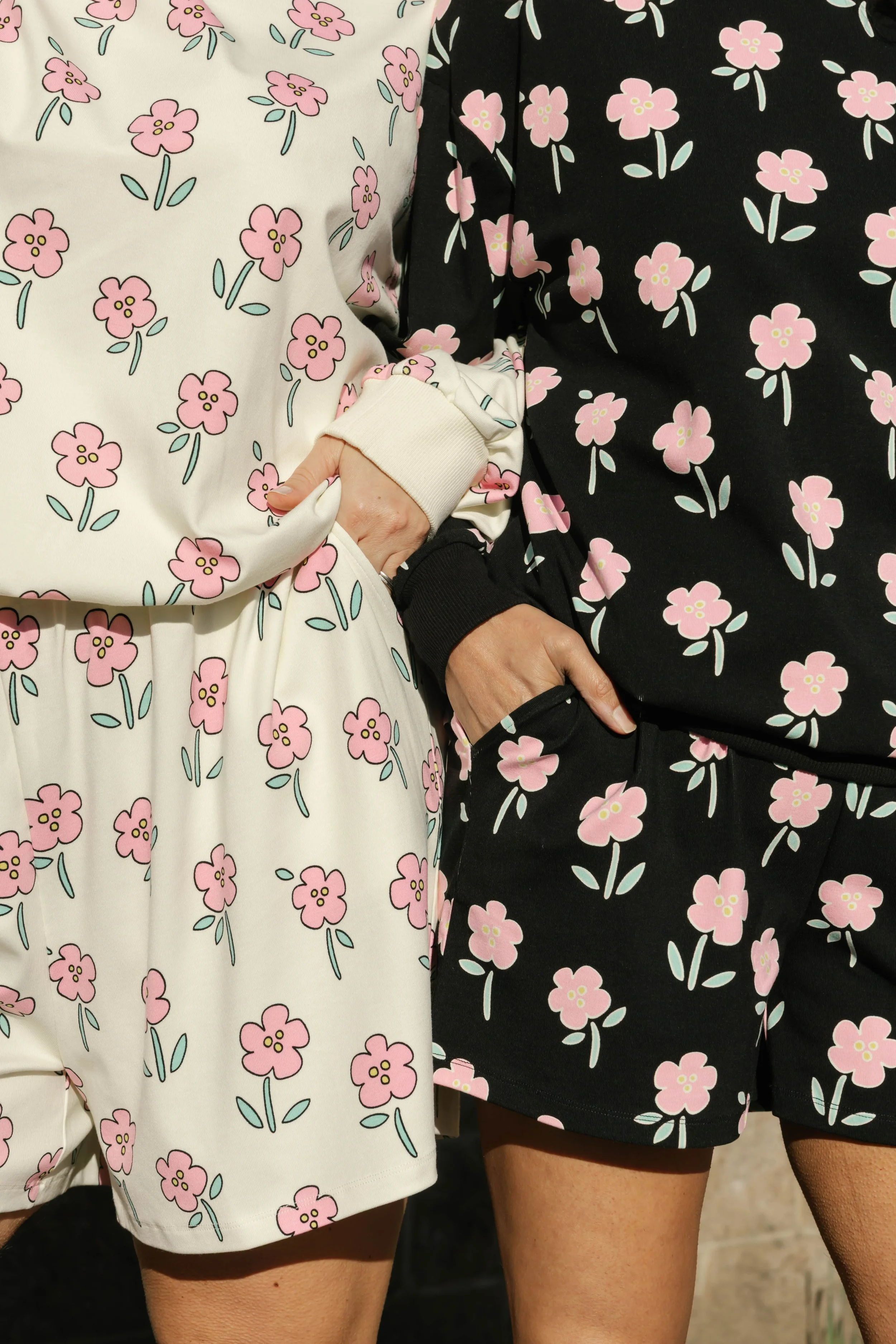 Close-up of two people wearing matching floral patterned clothing, with one person in black with pink flowers and the other in white with pink flowers. The focus is on their upper thighs and lower torsos.