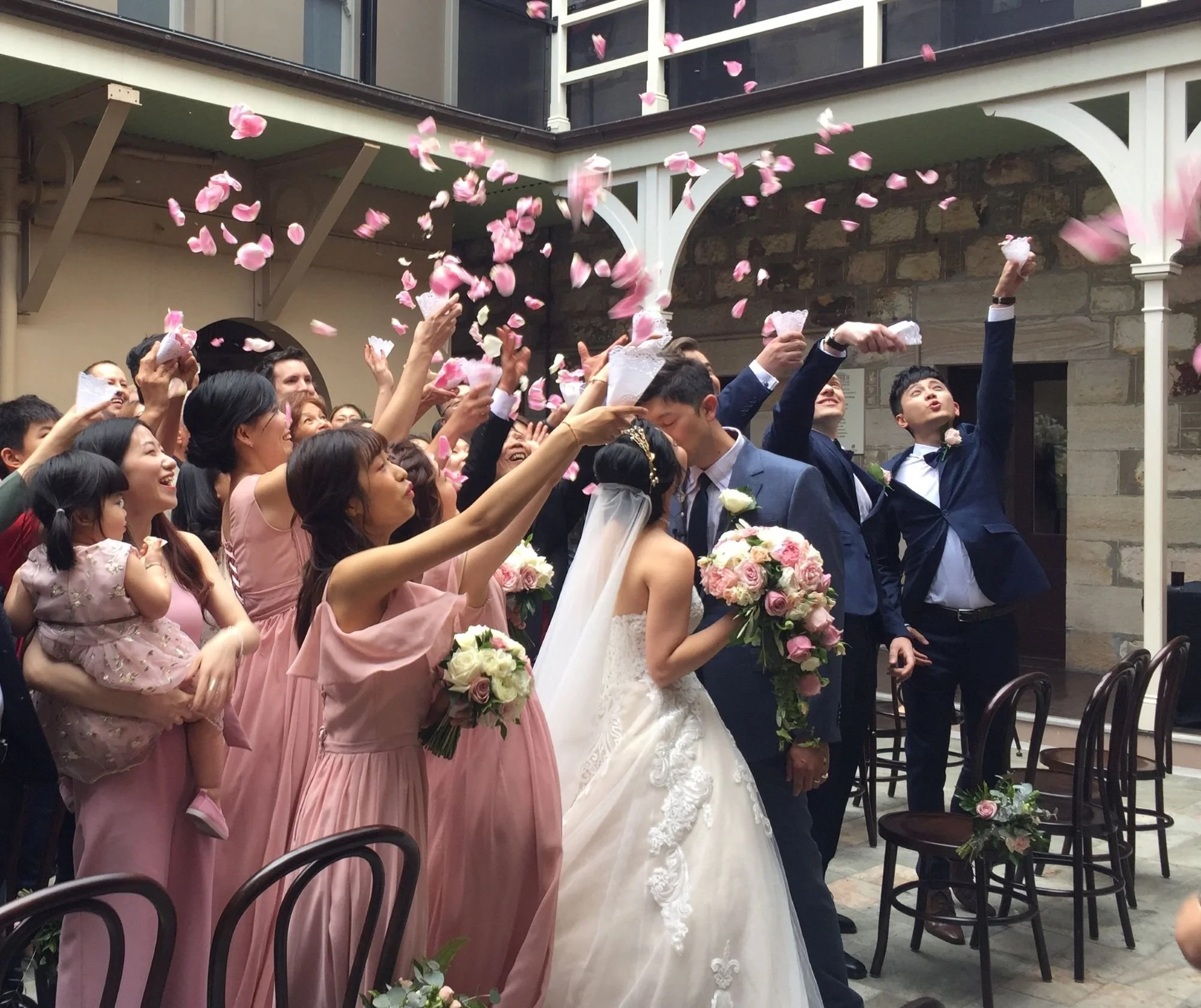 Wedding couple kiss while guests through petals in the air_Old Government House Courtyard Wedding