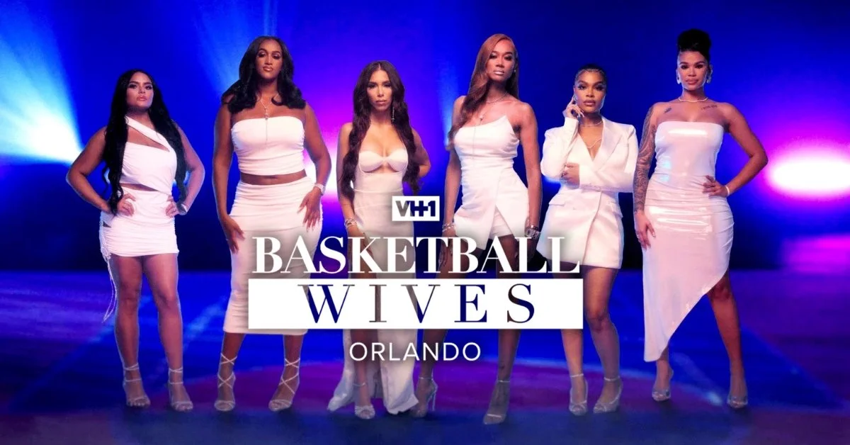Six women standing on a stage dressed in white outfits, with the text 'VH1 Basketball Wives Orlando' in front of them.