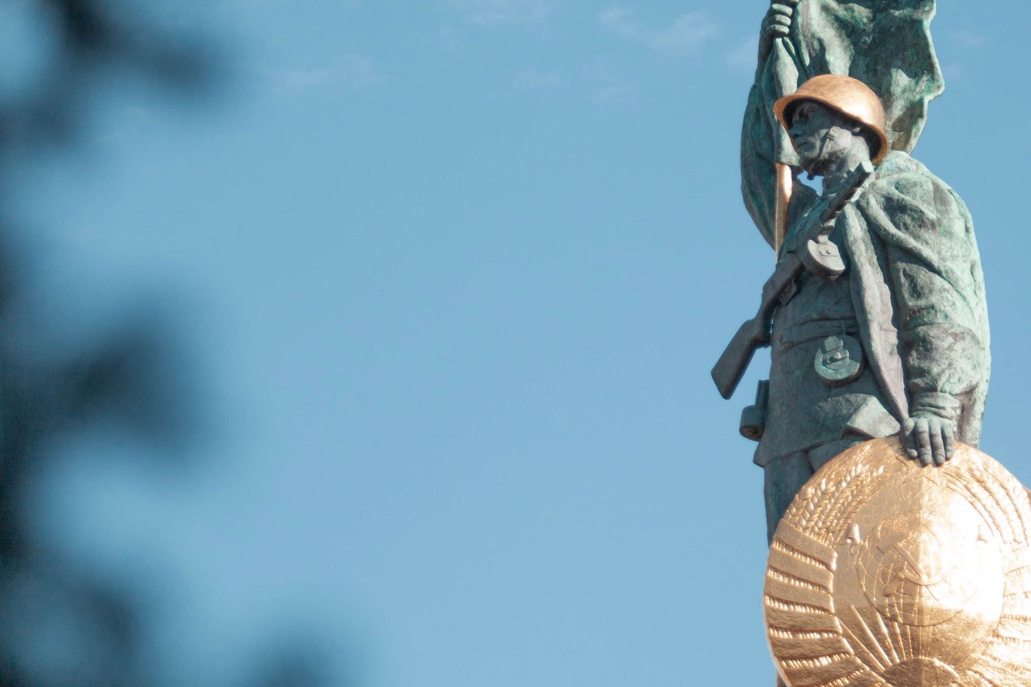 Blauer Himmel mit einem Detail des Sowjetischen Kriegerdenkmals Wien — Bronzeskulptur eines russischen Soldaten mit goldenem Helm und Schild, als Symbol für den Beginn des Kalten Krieges