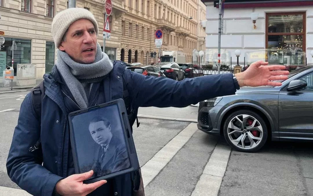 Vienna Guide Jascha Novak on his Spy tour. Holding an iPad with an historic photo of MI6 agent Peter Lunn. The walking tour guide is pointing at the Hotel Imperial on this cold February day