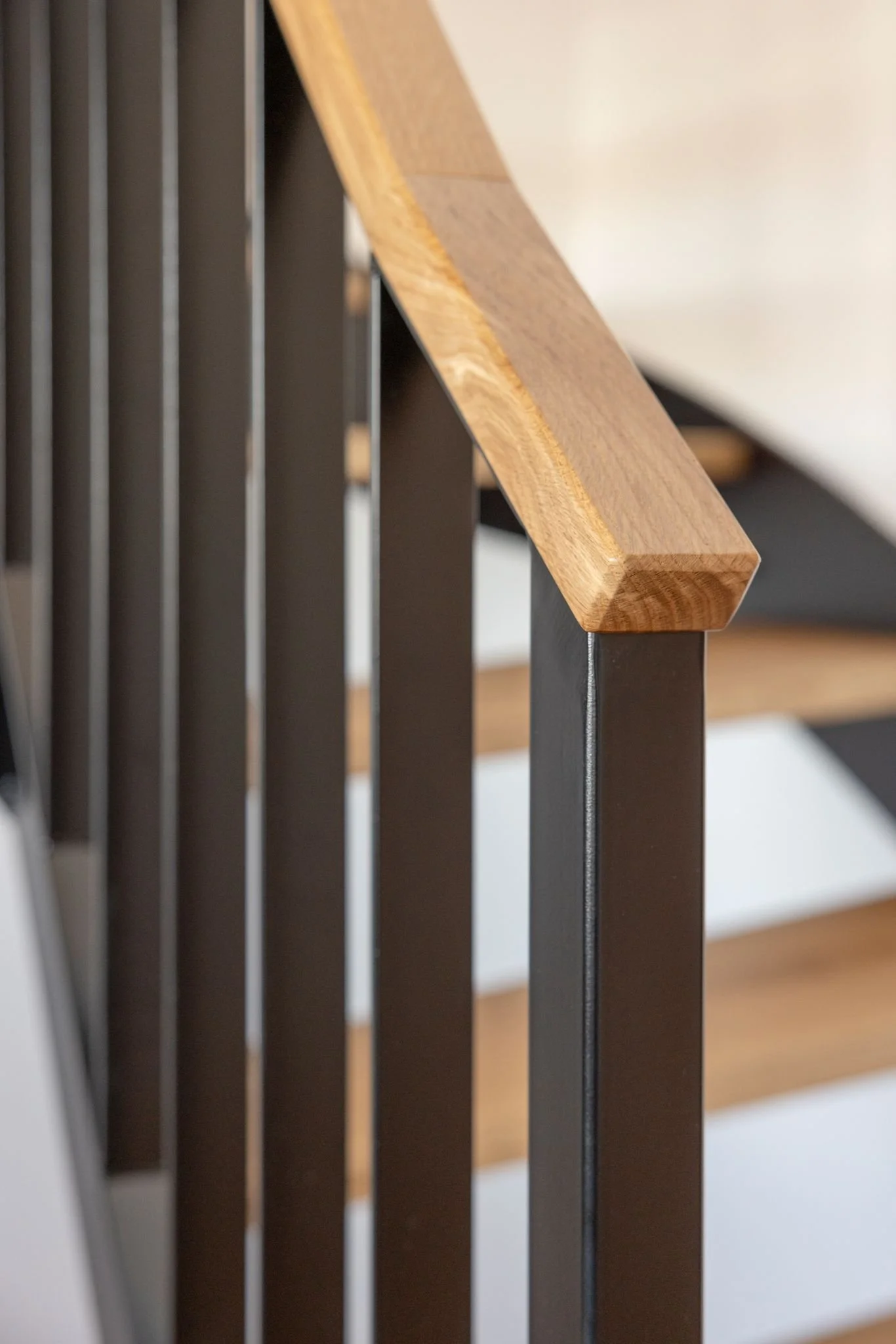 Nahaufnahme eines Stuhlrückenkopfes mit Holzarmlehne und schwarzen Metallstangen.